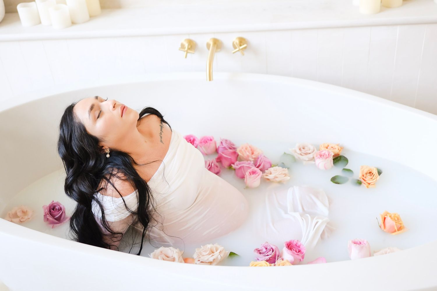 A serene milk bath photography session with scattered pink and peach roses floating on white creamy water.