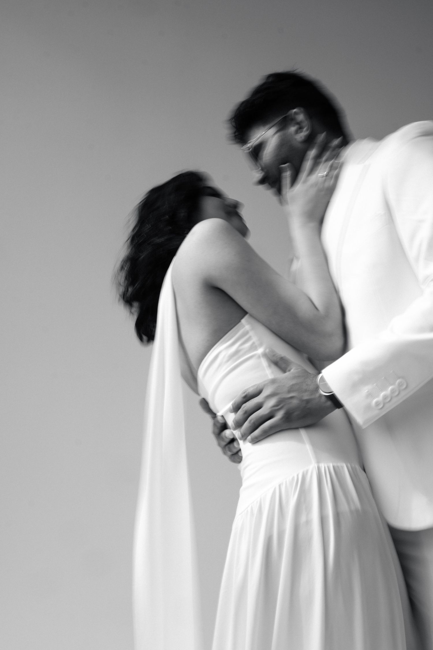 Black and white photo of bride and groom in an intimate embrace, groom in white suit holding bride close.