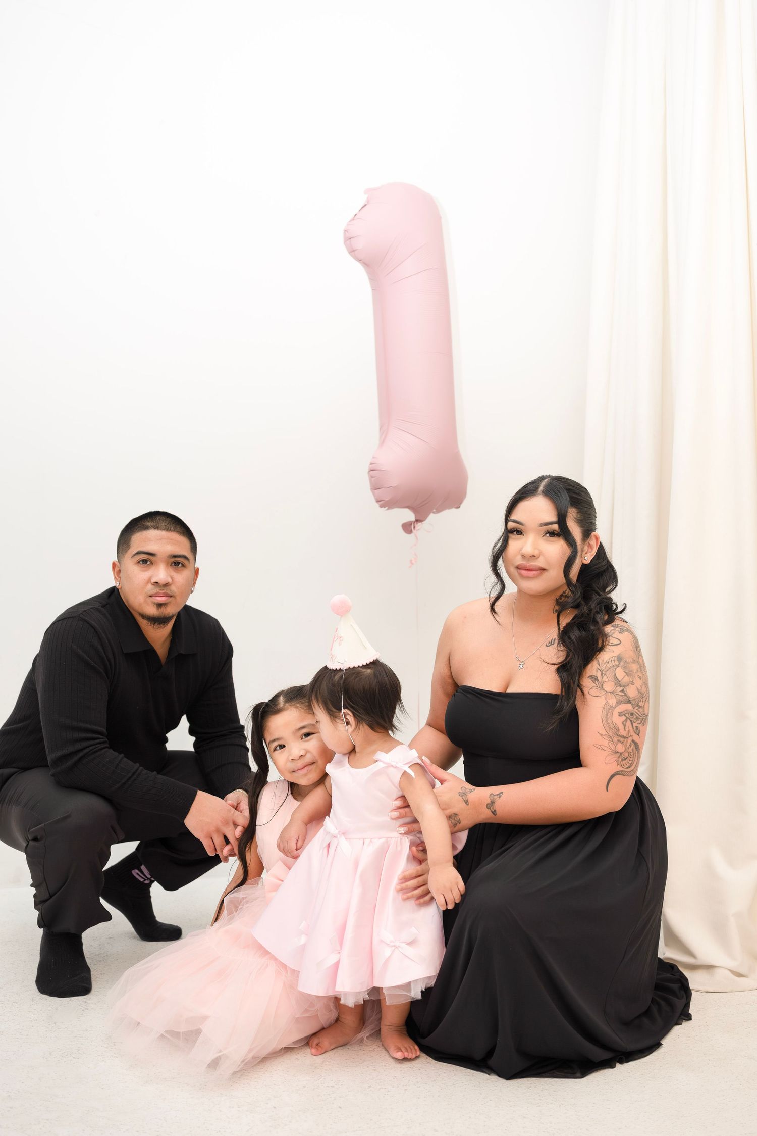 Family of four posing with a pink number one balloon, celebrating a baby girl's first birthday in matching outfits.