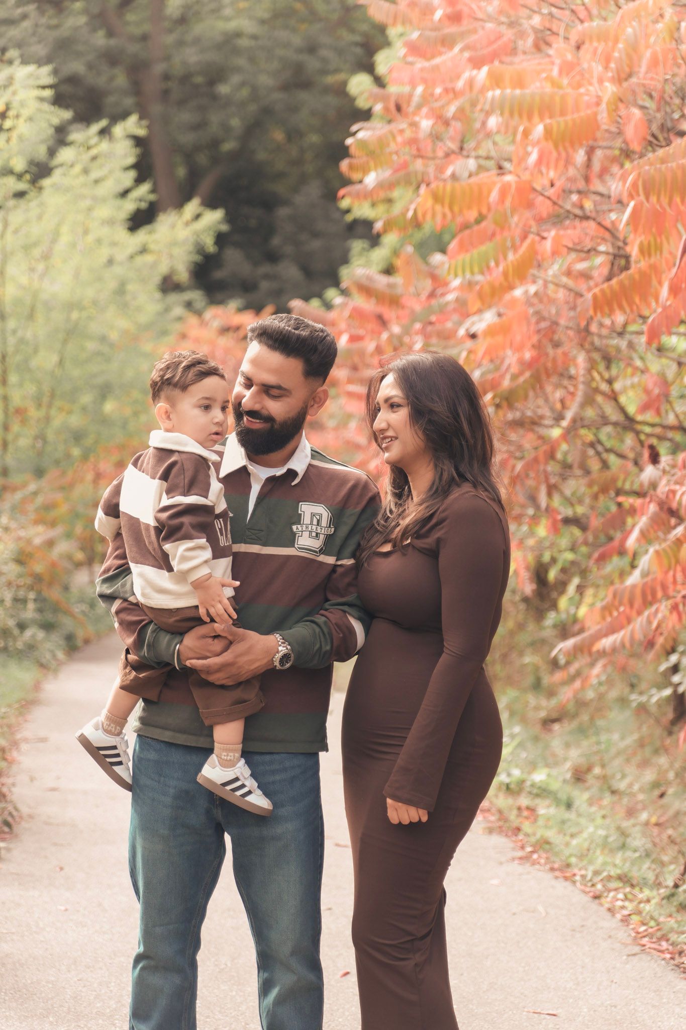 A family enjoys a fall day together on a path with vibrant orange autumn foliage in the background.