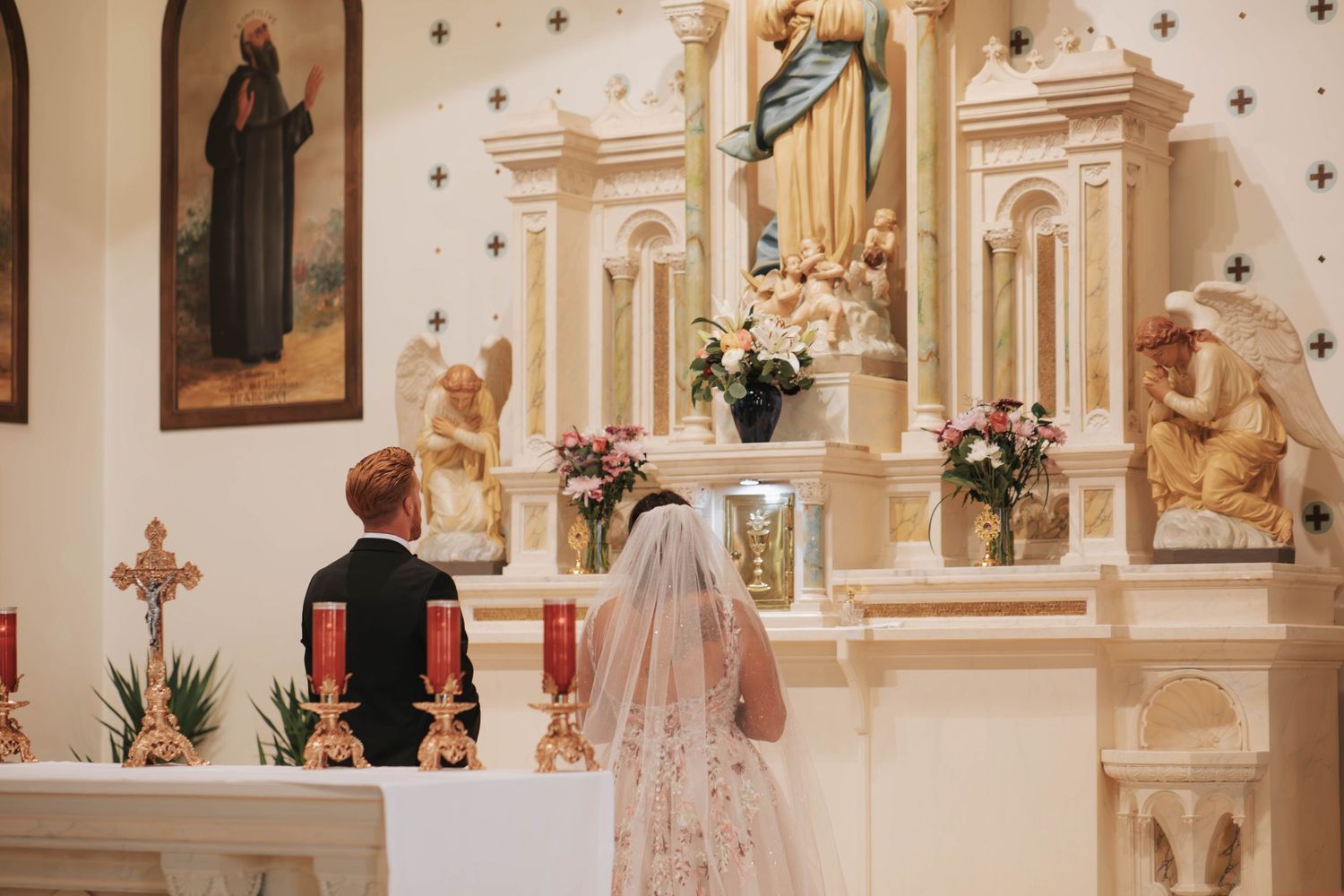 Newlywed couple kneeling in front of a statue of Mary blessing their marriage