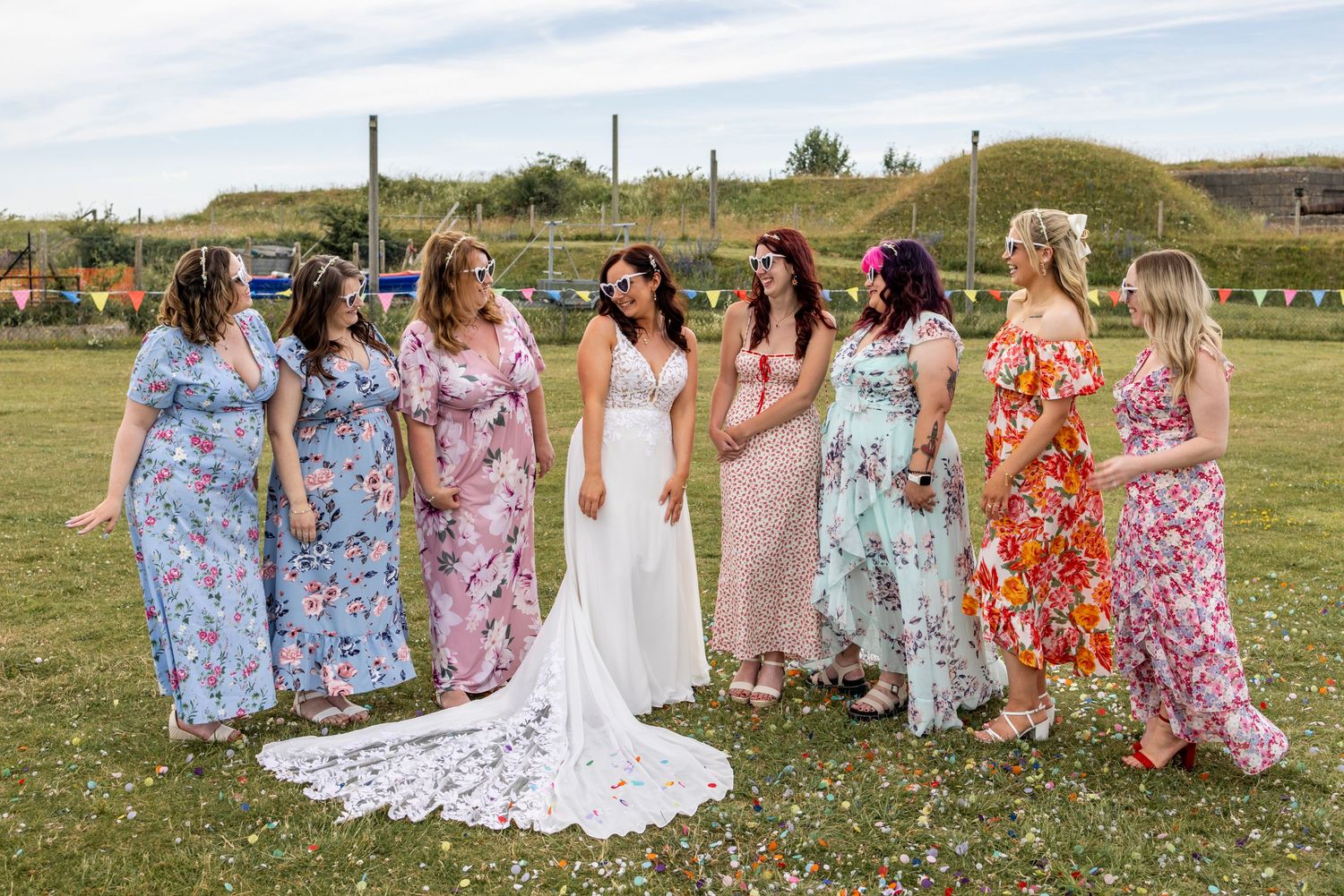 Bridal party in floral dresses poses outdoors on a sunny day.