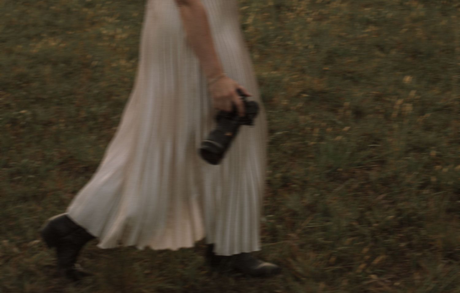woman walking through a field holding a camera with soft motion blur and nostalgic film-inspired tones in Charlotte