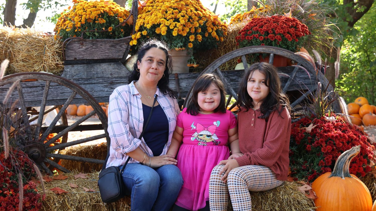 Fall family portrait with rustic wagon wheel display and pumpkins surrounded by colorful mums.
