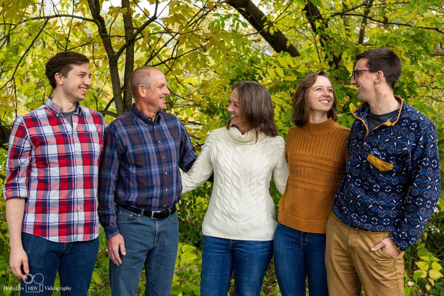 Family group standing together outdoors with yellow fall foliage in background.