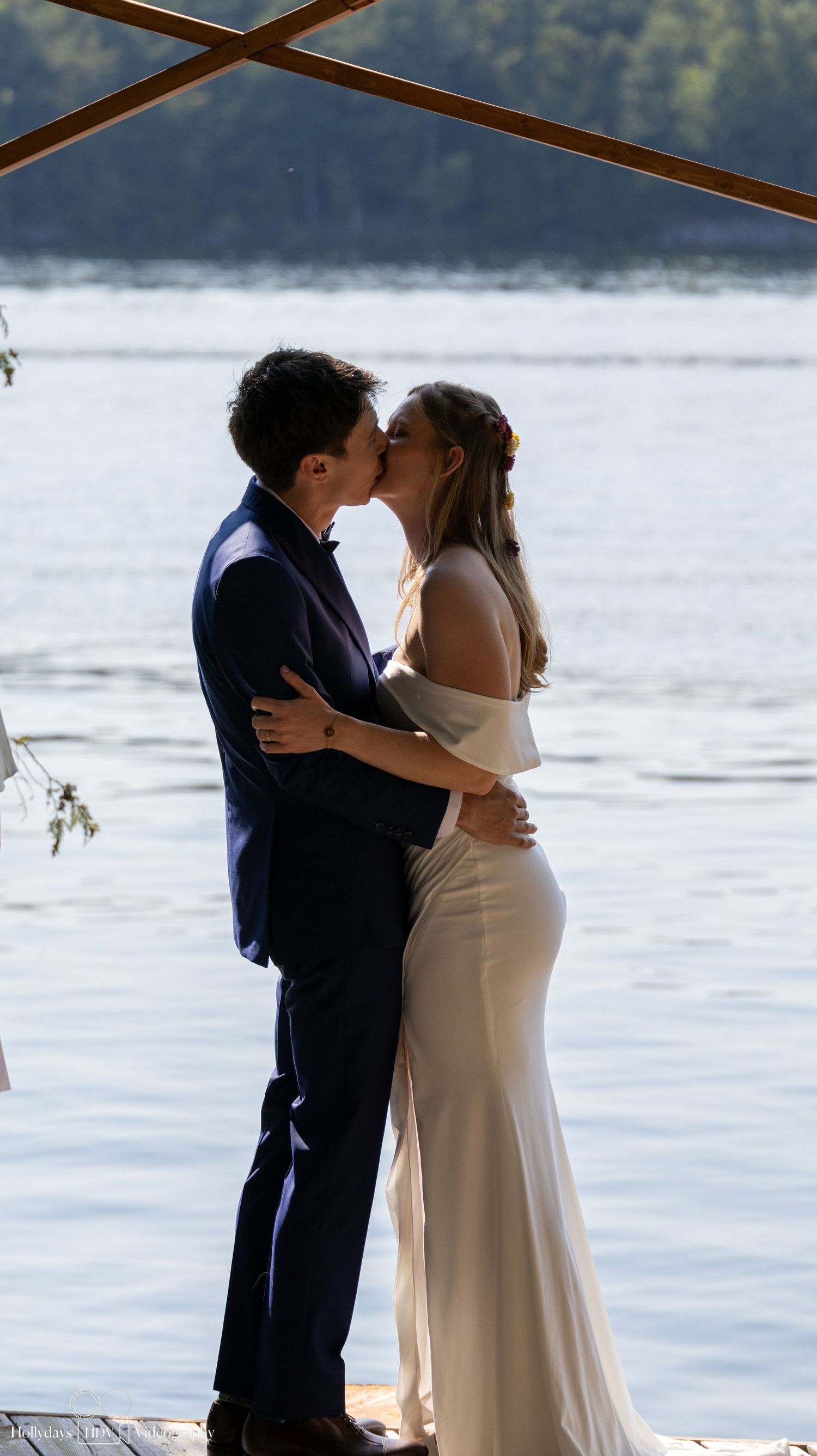 A couple embraces during their first kiss as newlyweds at a scenic lakeside ceremony.