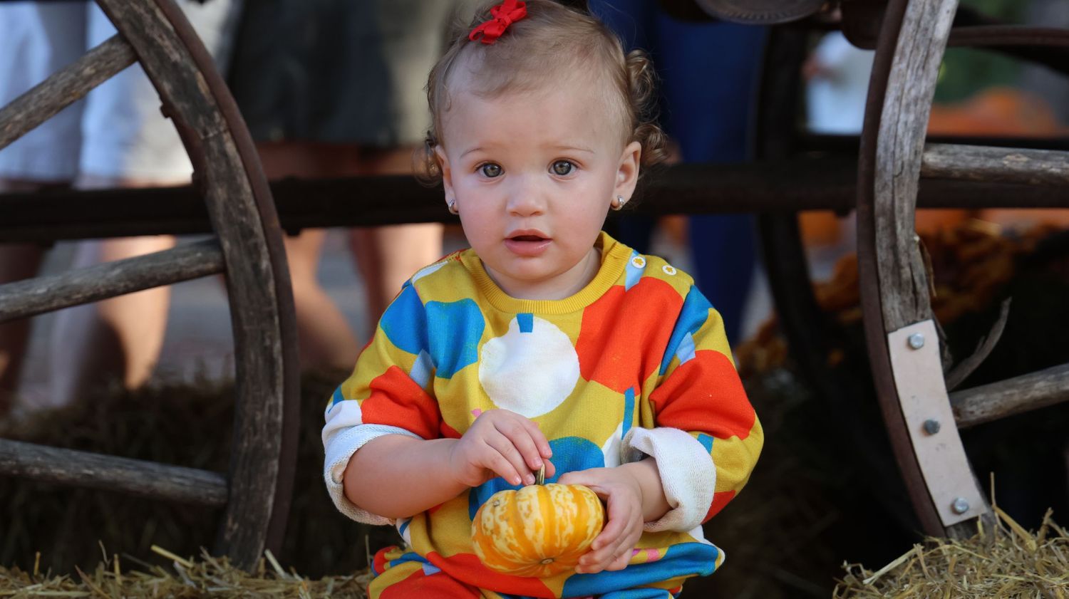 Small child in colorful tie-dye shirt holding a plush toy near wooden furniture.