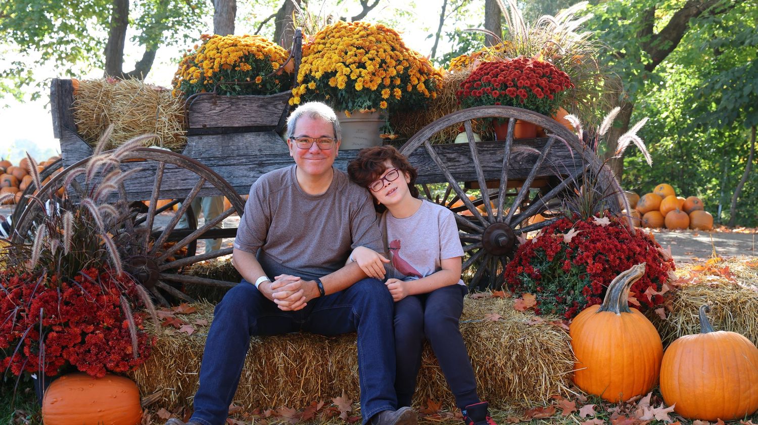 Couple sitting on hay bales with autumn decorations and orange pumpkins.