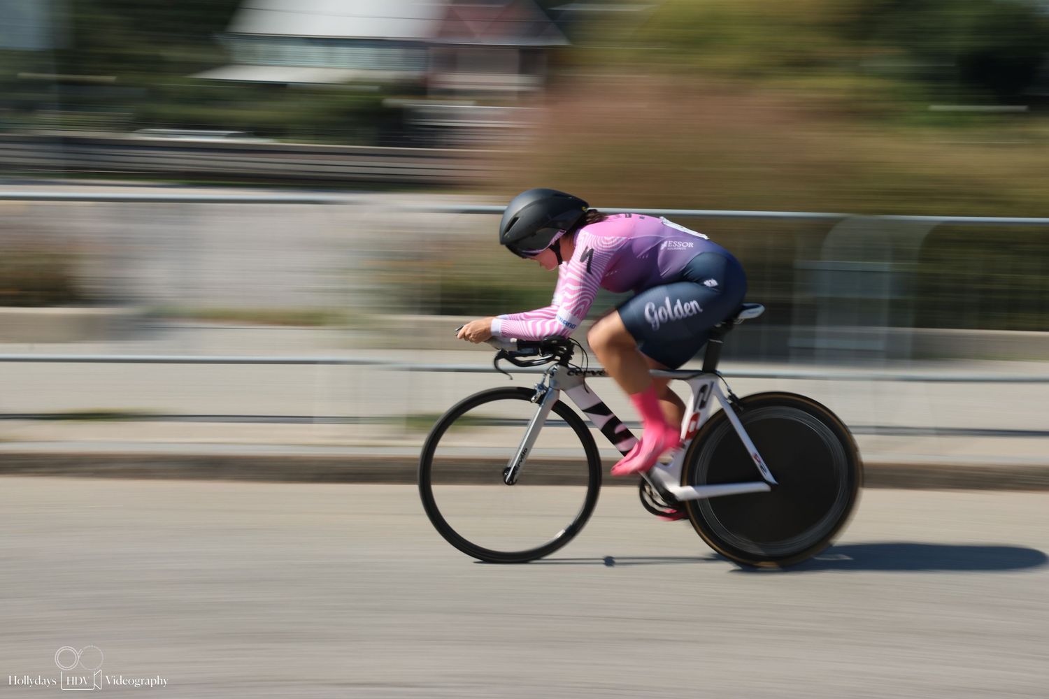 Motion blurred cyclist in pink jersey racing on time trial bike during competitive cycling event.