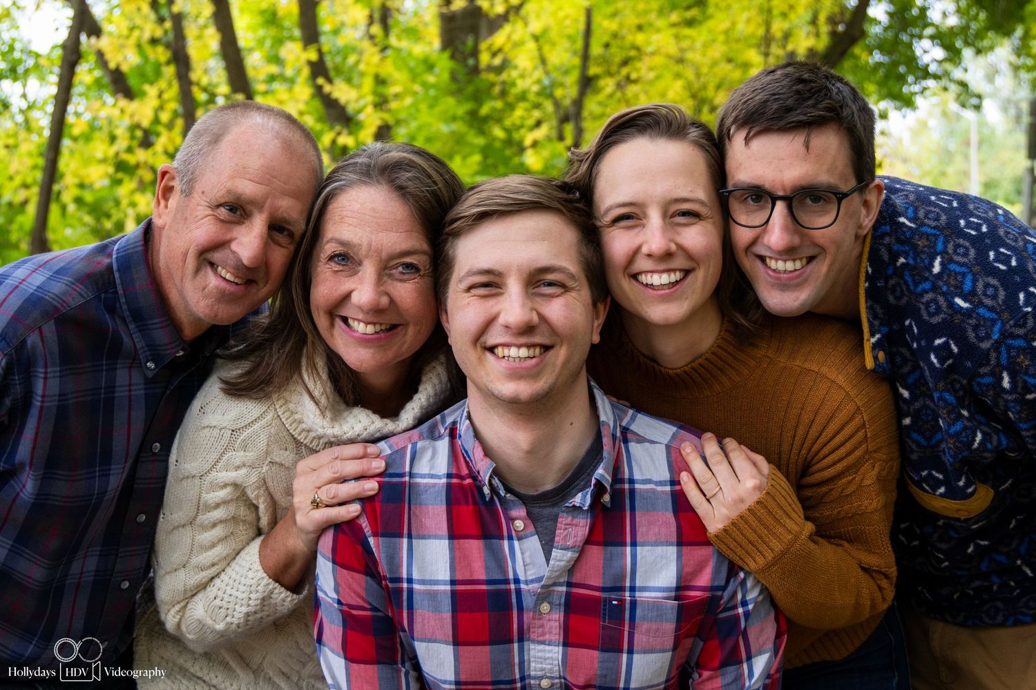 Family group photo with everyone smiling outdoors in natural setting.