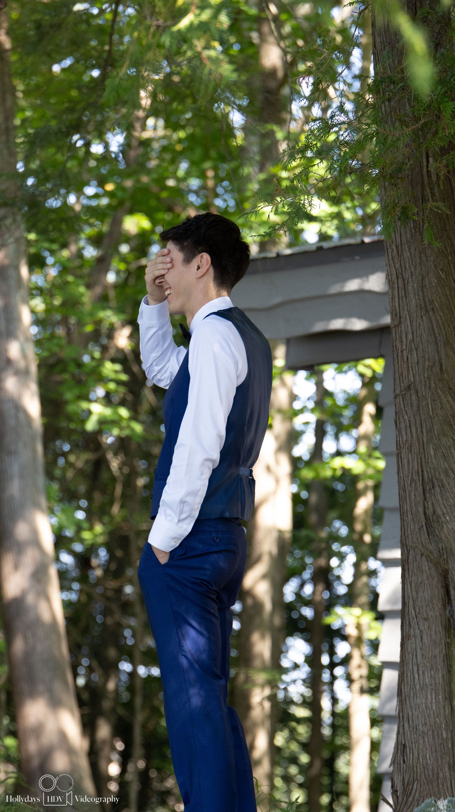 Person in formal navy vest and white shirt poses against woodland backdrop.