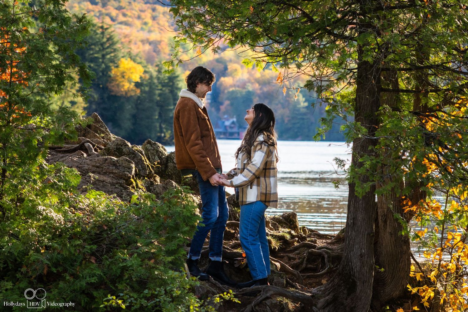 Couple standing on tree roots overlooking a scenic lake during autumn.