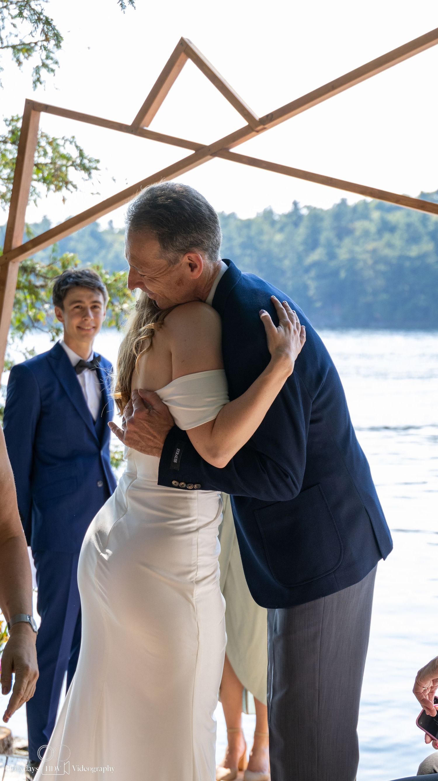 An emotional moment during a lakeside wedding ceremony under a wooden altar structure.