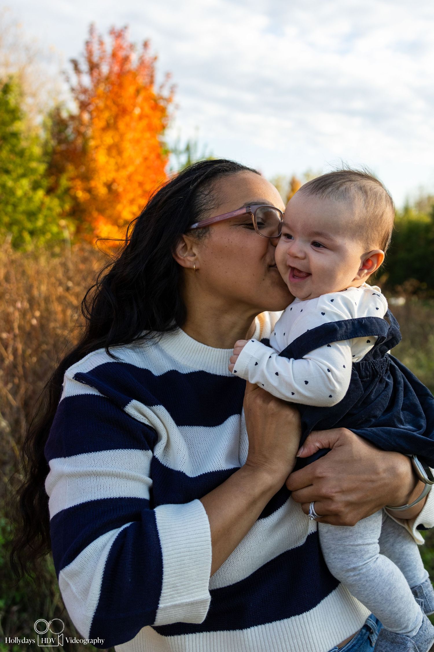 Sweet moment between parent and baby with vibrant fall foliage in background.