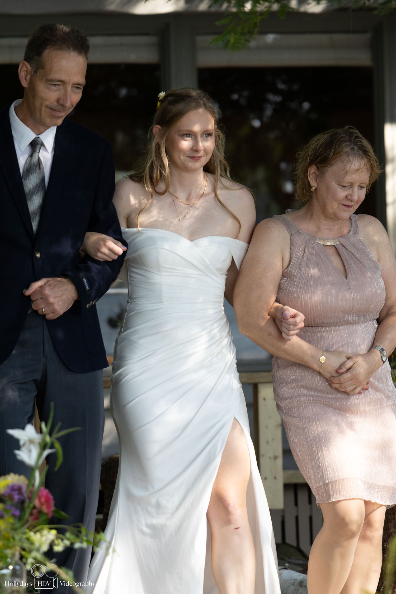 A wedding party walks together on a sunny day during an outdoor celebration.
