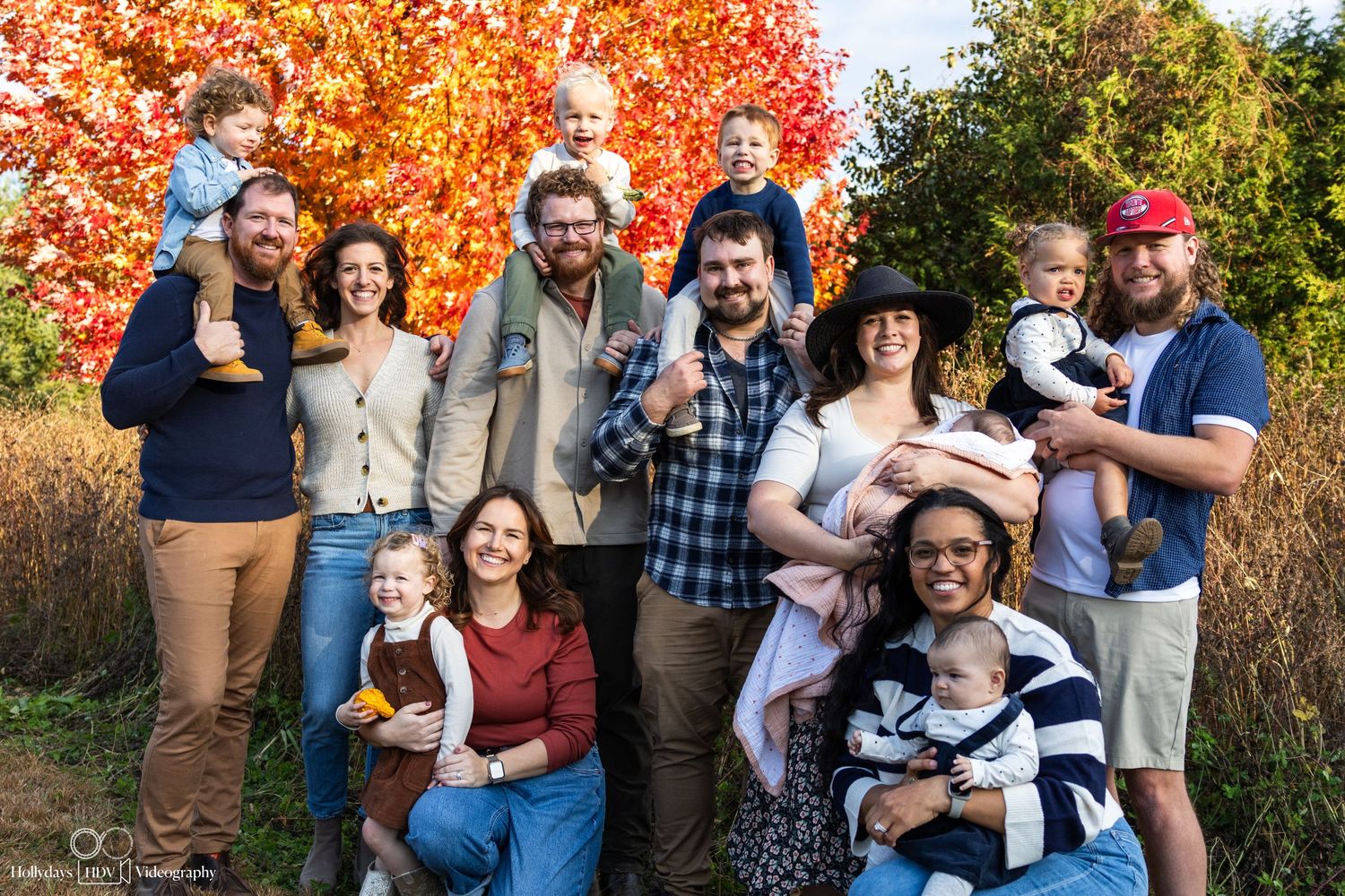 Large family group photo with colorful autumn trees in background.