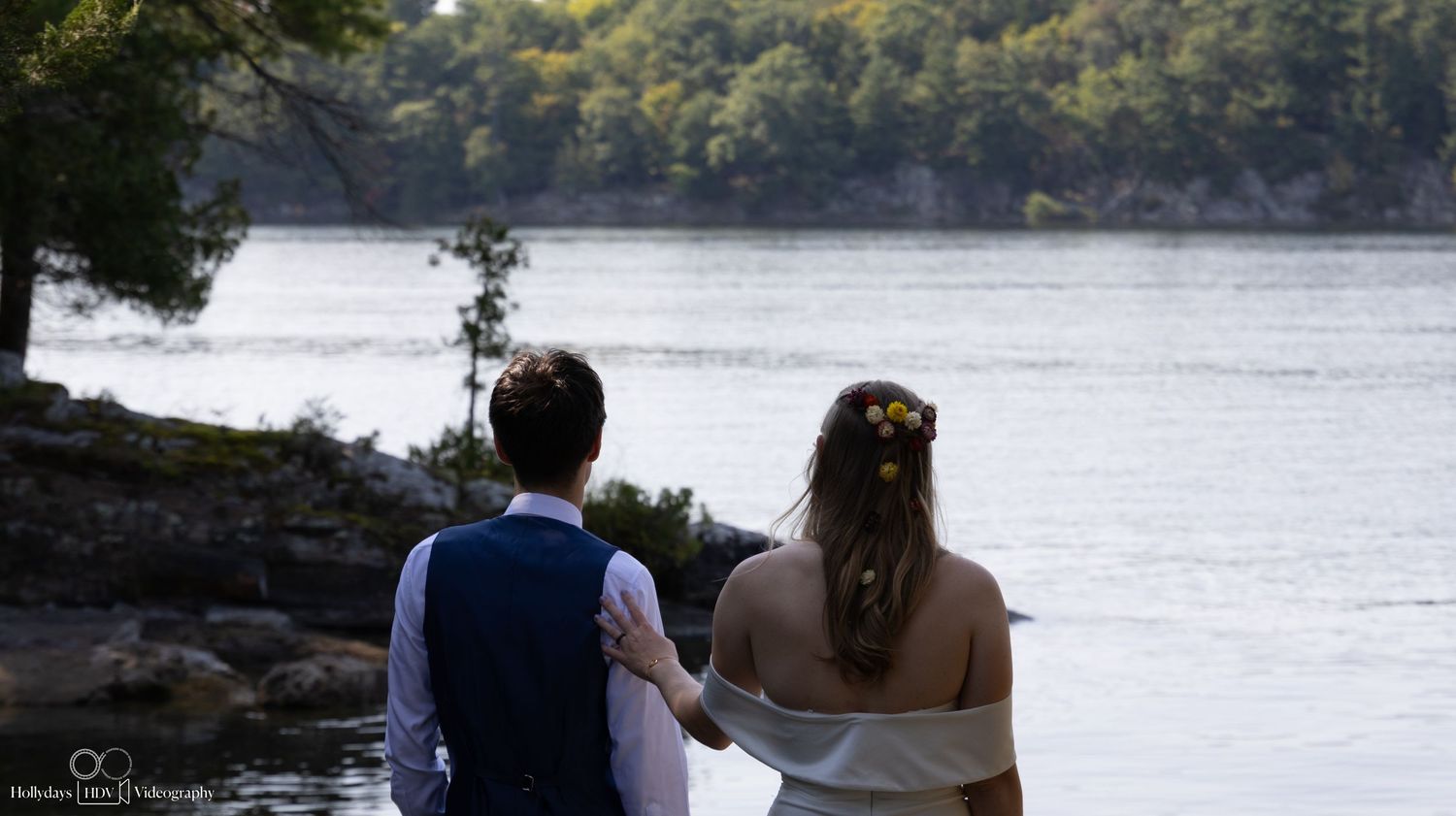 Couple gazes at scenic lake view from rocky shoreline.