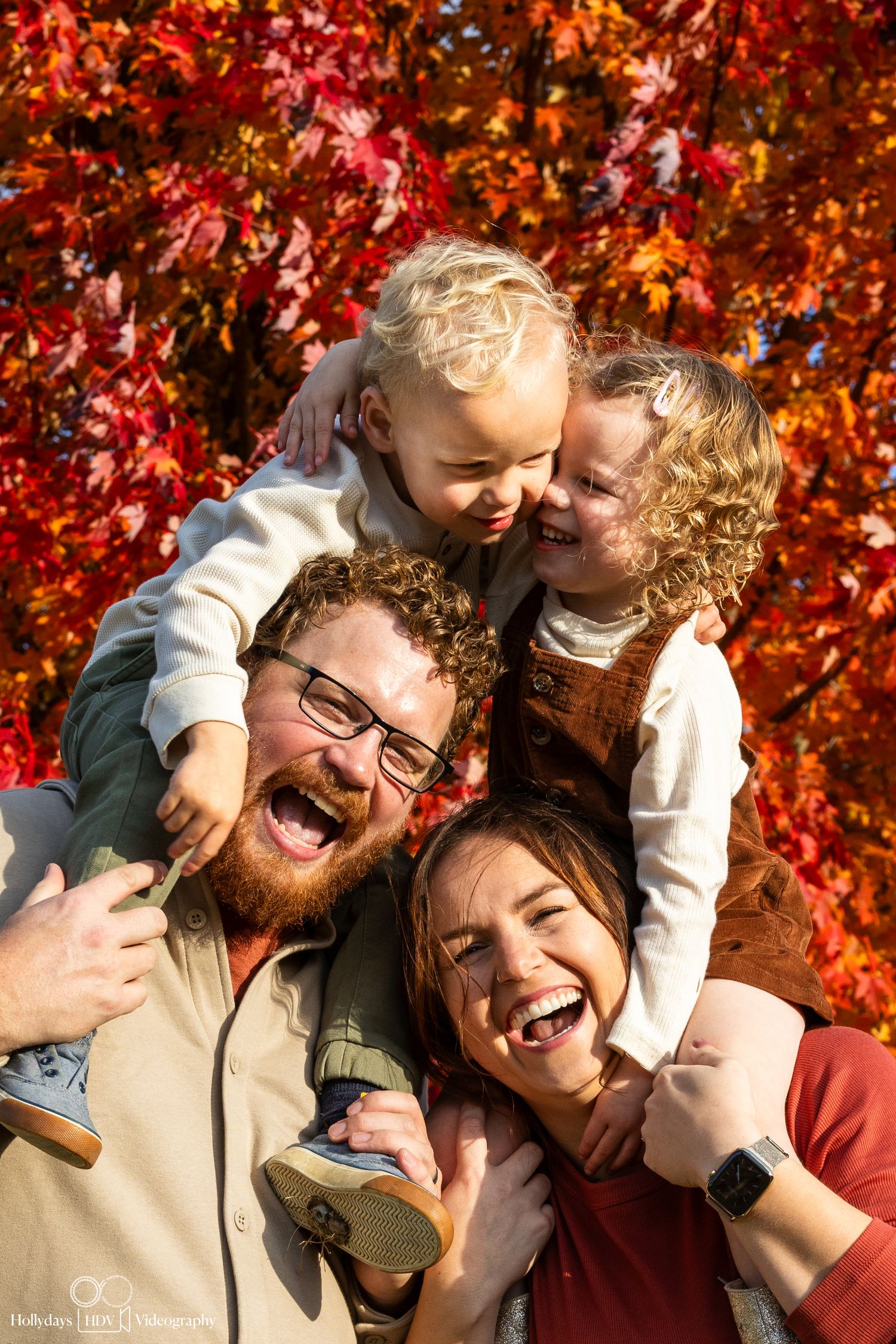 Joyful family pile-up portrait with vibrant red autumn leaves in background.