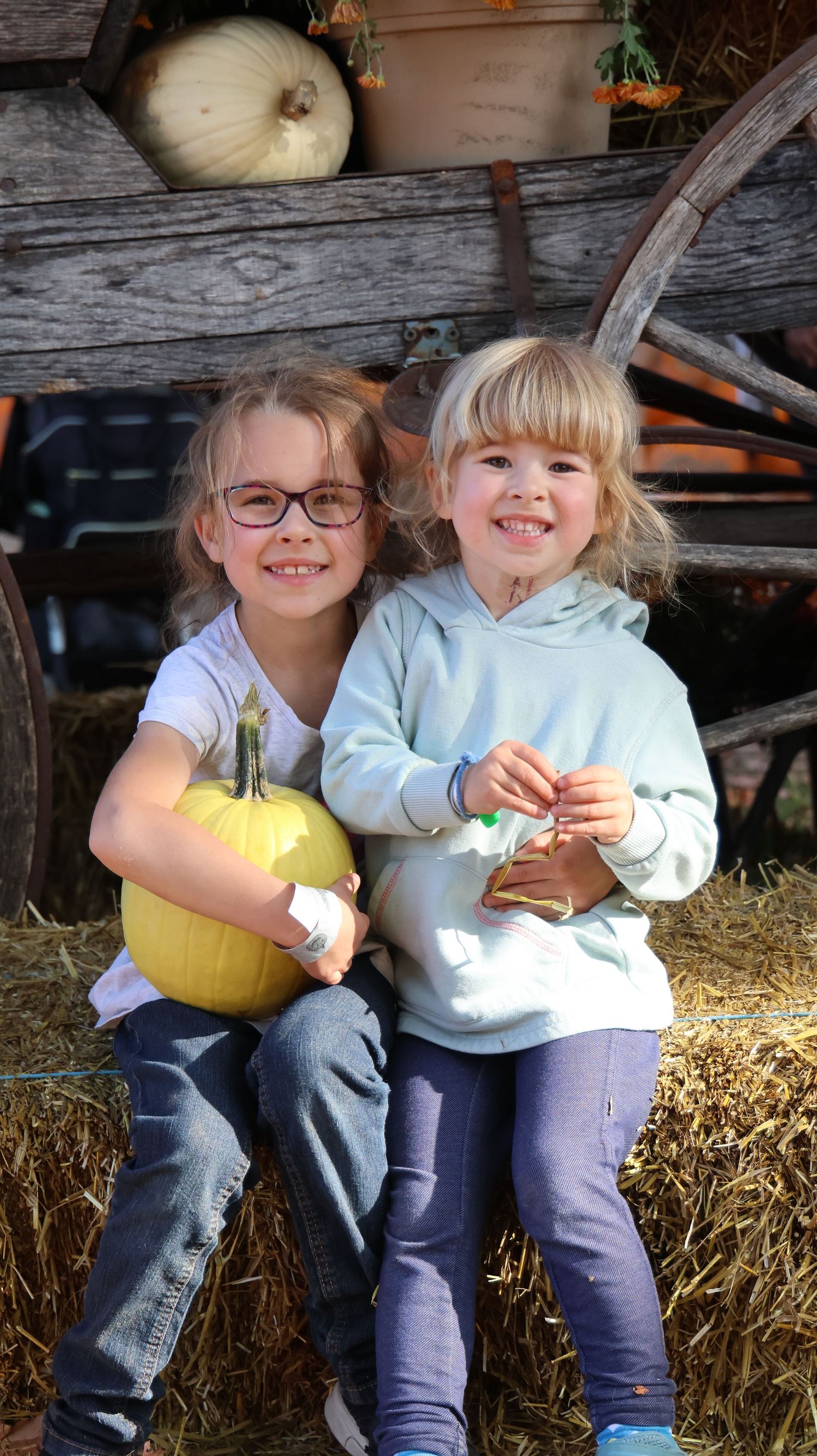 Two children sitting on hay bales with pumpkins during autumn photo session.