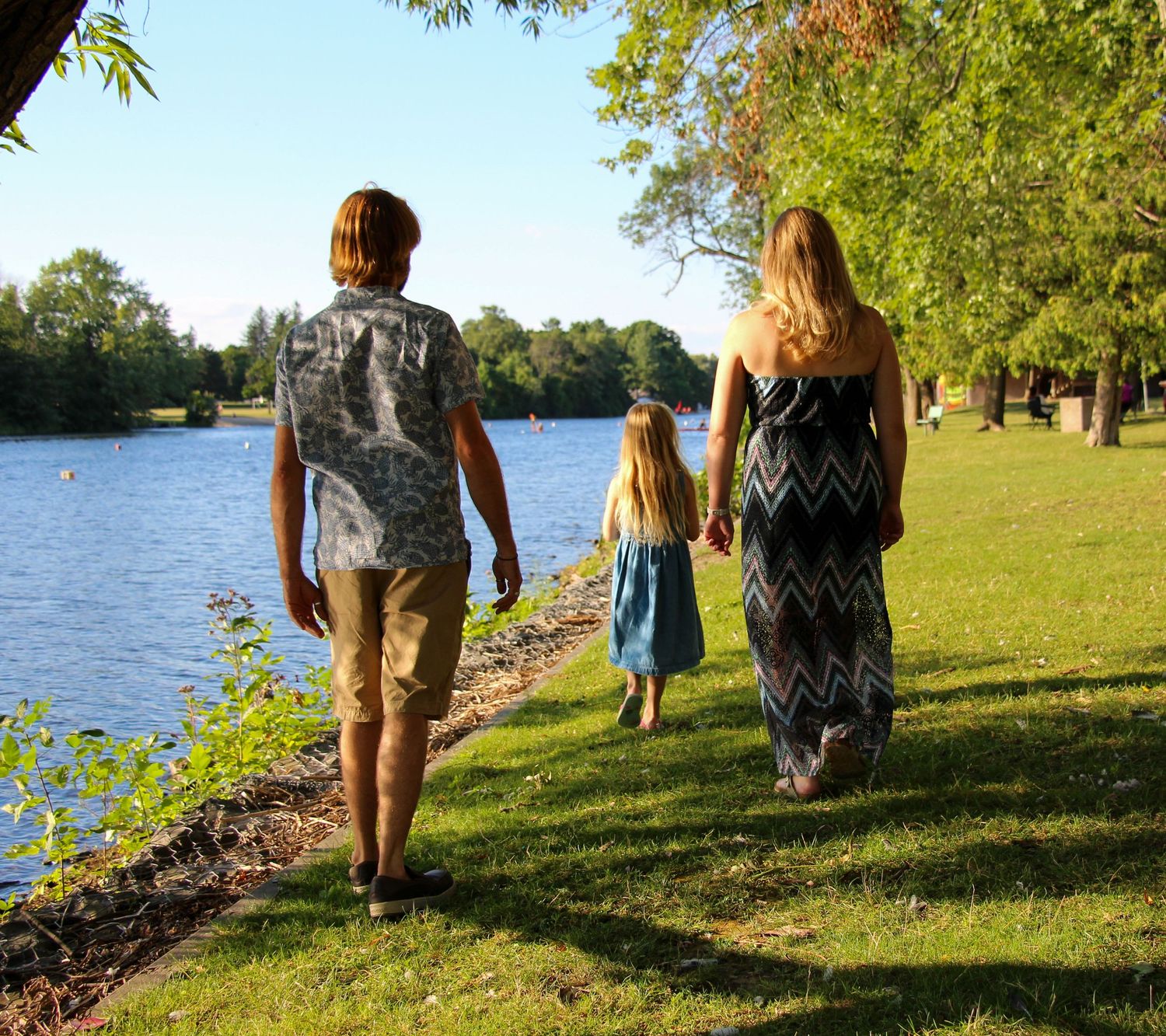 Three people walking along a lakeside path on a sunny day.