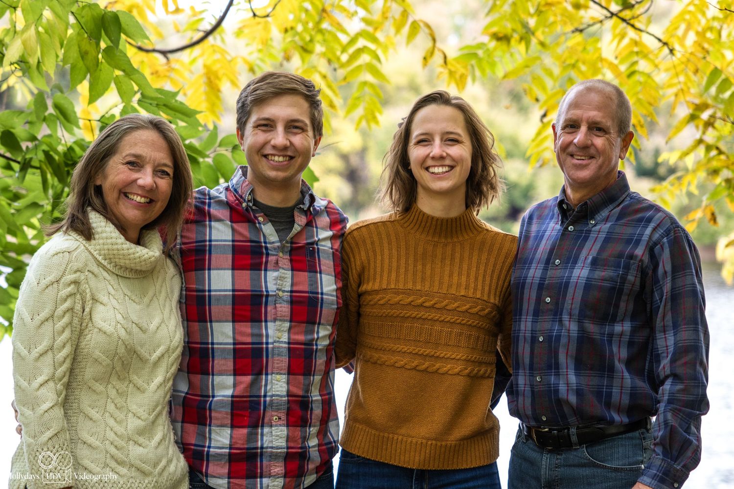 Group portrait of family members wearing sweaters and casual attire in autumn setting.