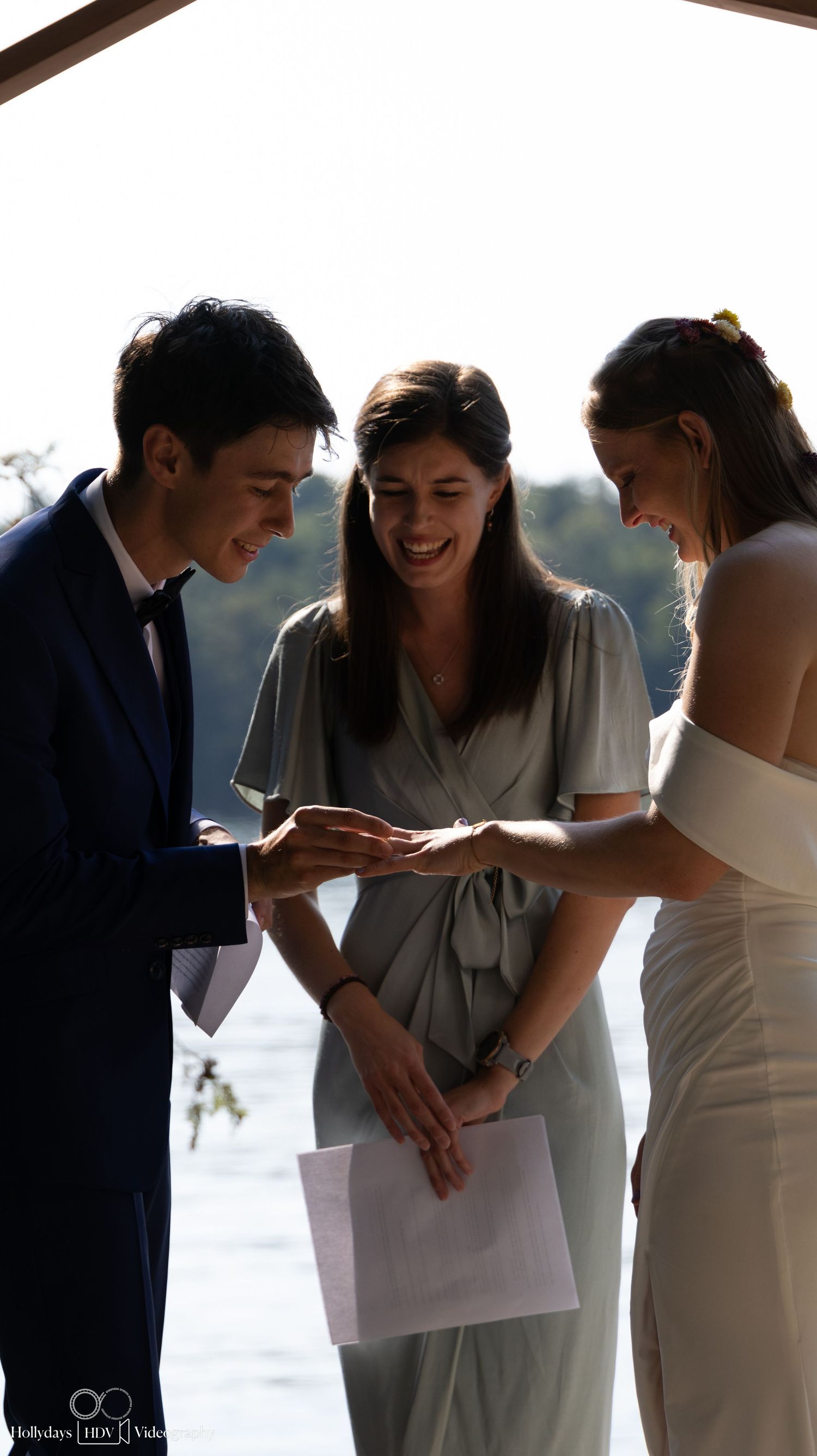 A lakeside wedding ceremony with participants sharing a joyful moment under wooden beams.