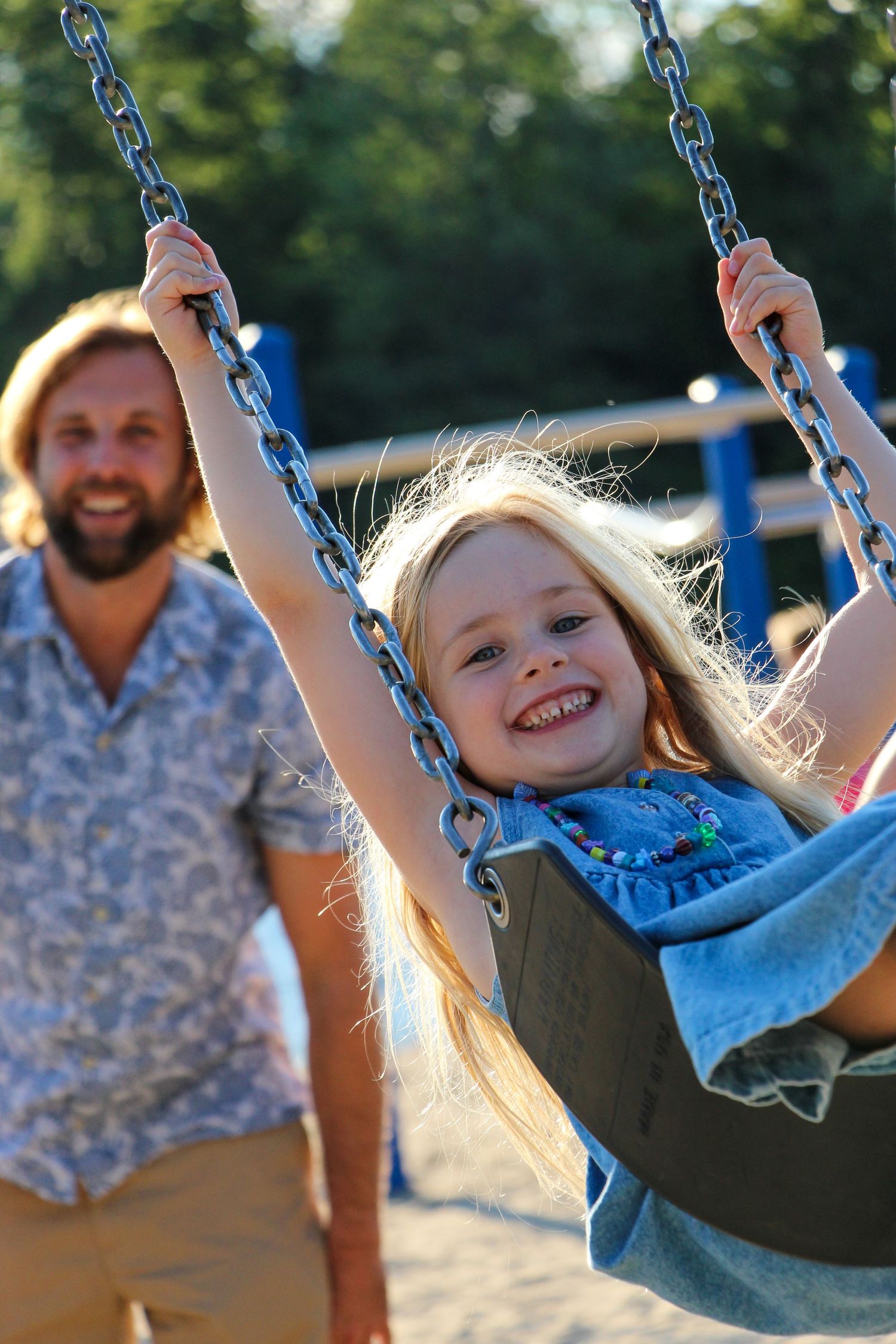 Child swinging joyfully on playground equipment during a sunny afternoon.
