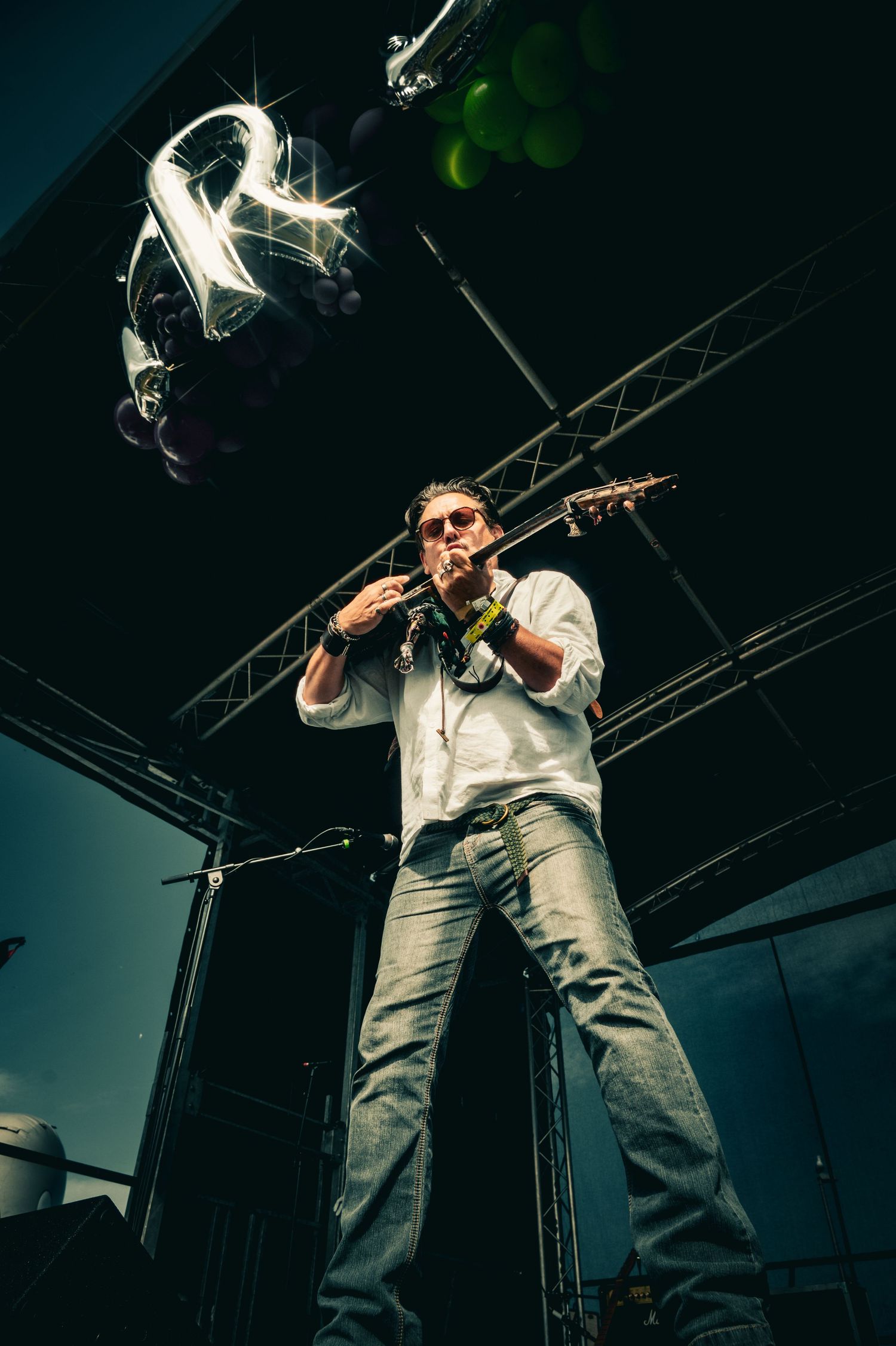 A male musician plays violin on stage beneath glowing letter R balloons at a live event.