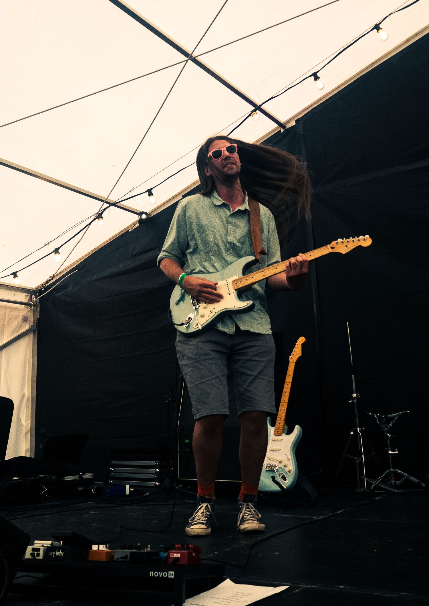 Guitarist performing on stage with a vintage Fender guitar under tent lighting.