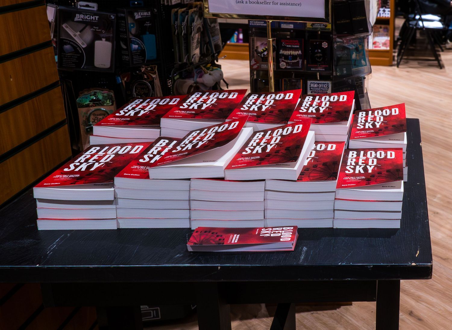 Stacks of Blood Sky books displayed on a dark table at a bookstore event or signing.