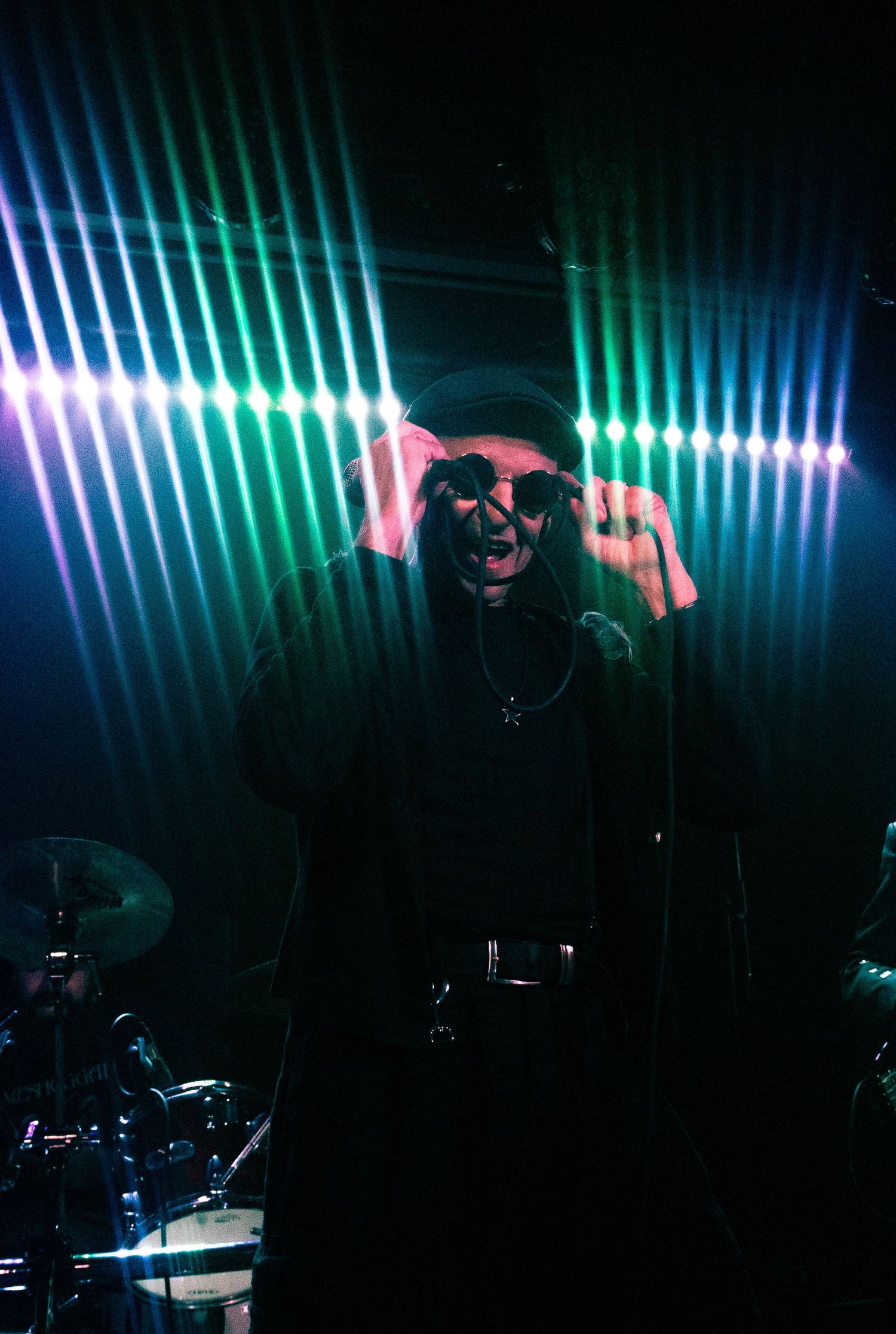 Performer in dramatic pose against geometric light display during concert performance.