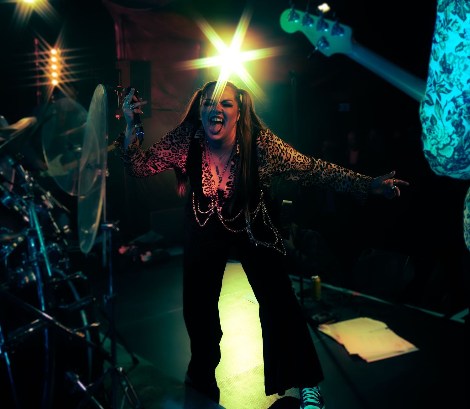 Dramatic concert performance on dark stage with bright spotlights and turquoise lighting effects in the background.