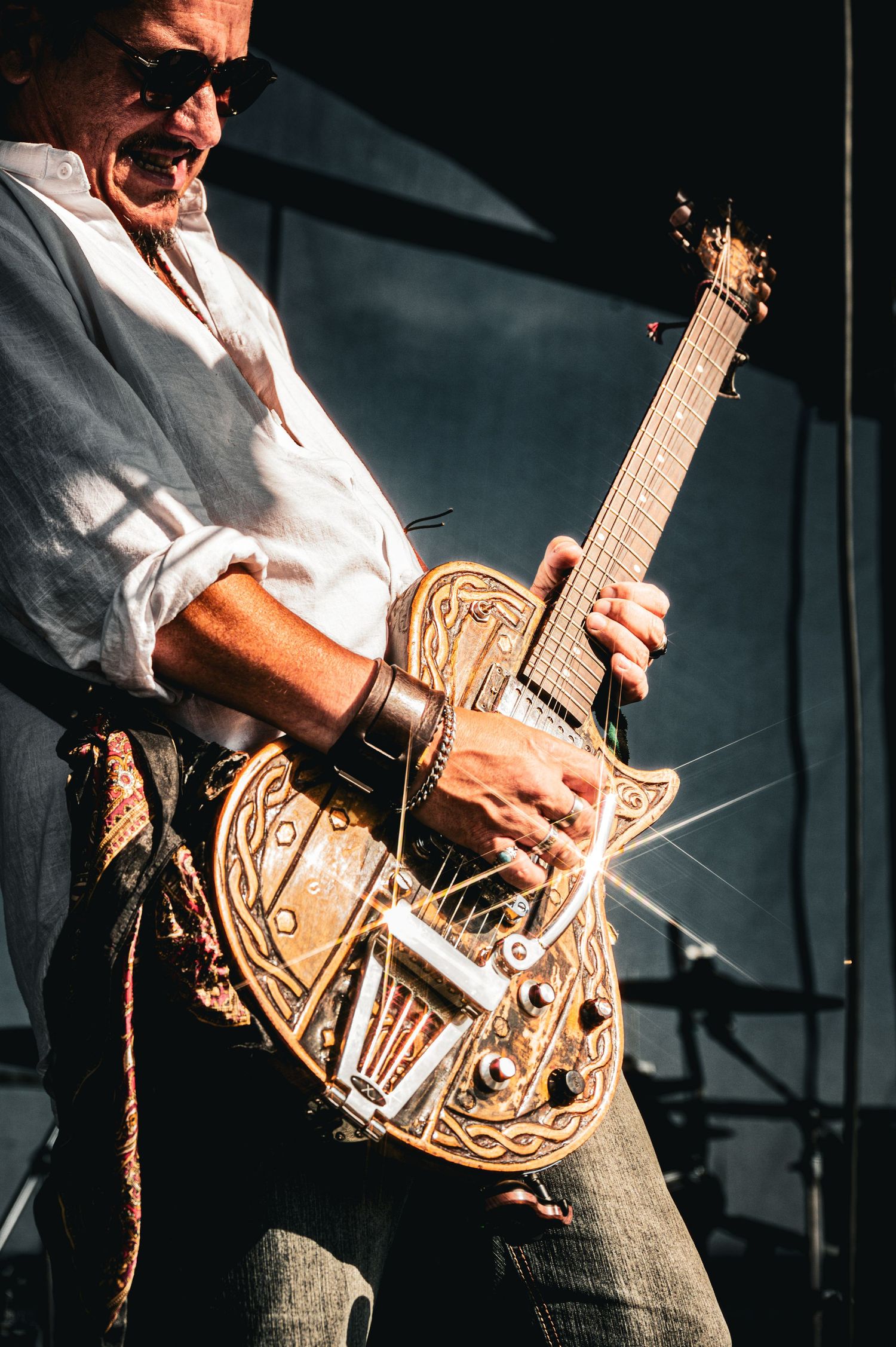 Musician playing an ornate leather-decorated electric guitar on stage with sparkling light effects.