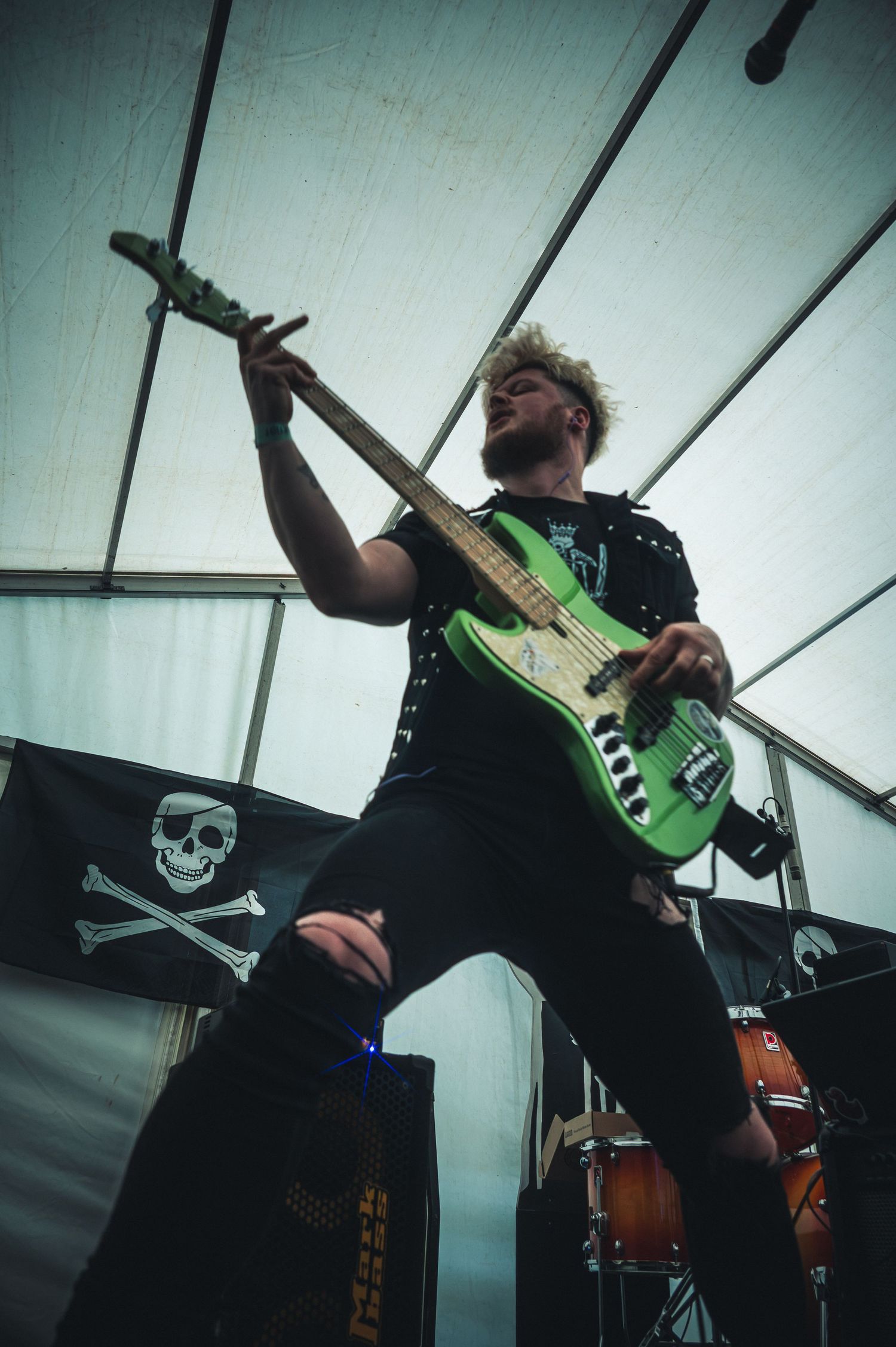 Guitarist playing green electric guitar on stage with pirate flag backdrop at live music event.
