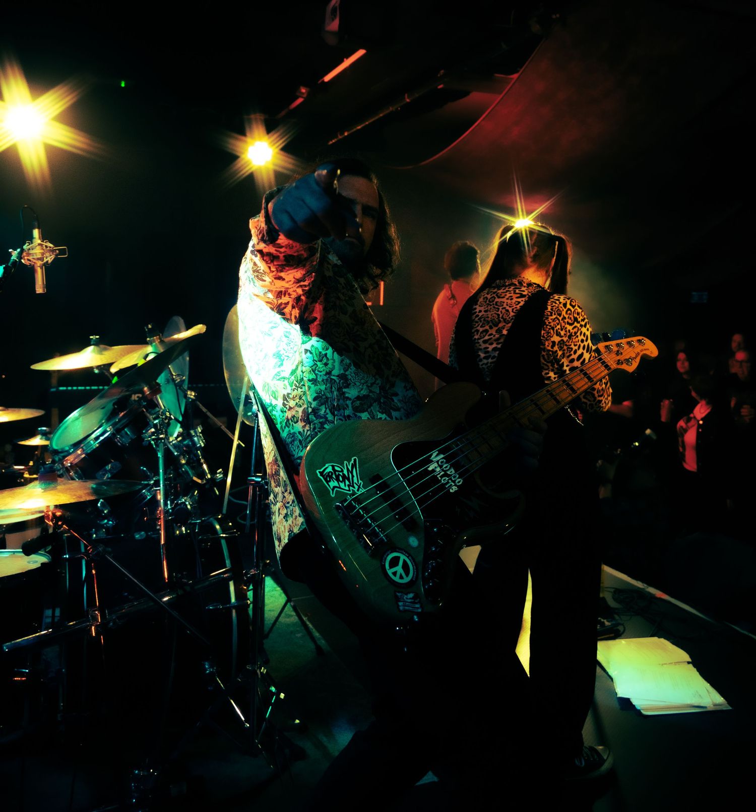 Musicians performing on stage at a dimly lit club with dramatic lighting effects creating a moody atmosphere.