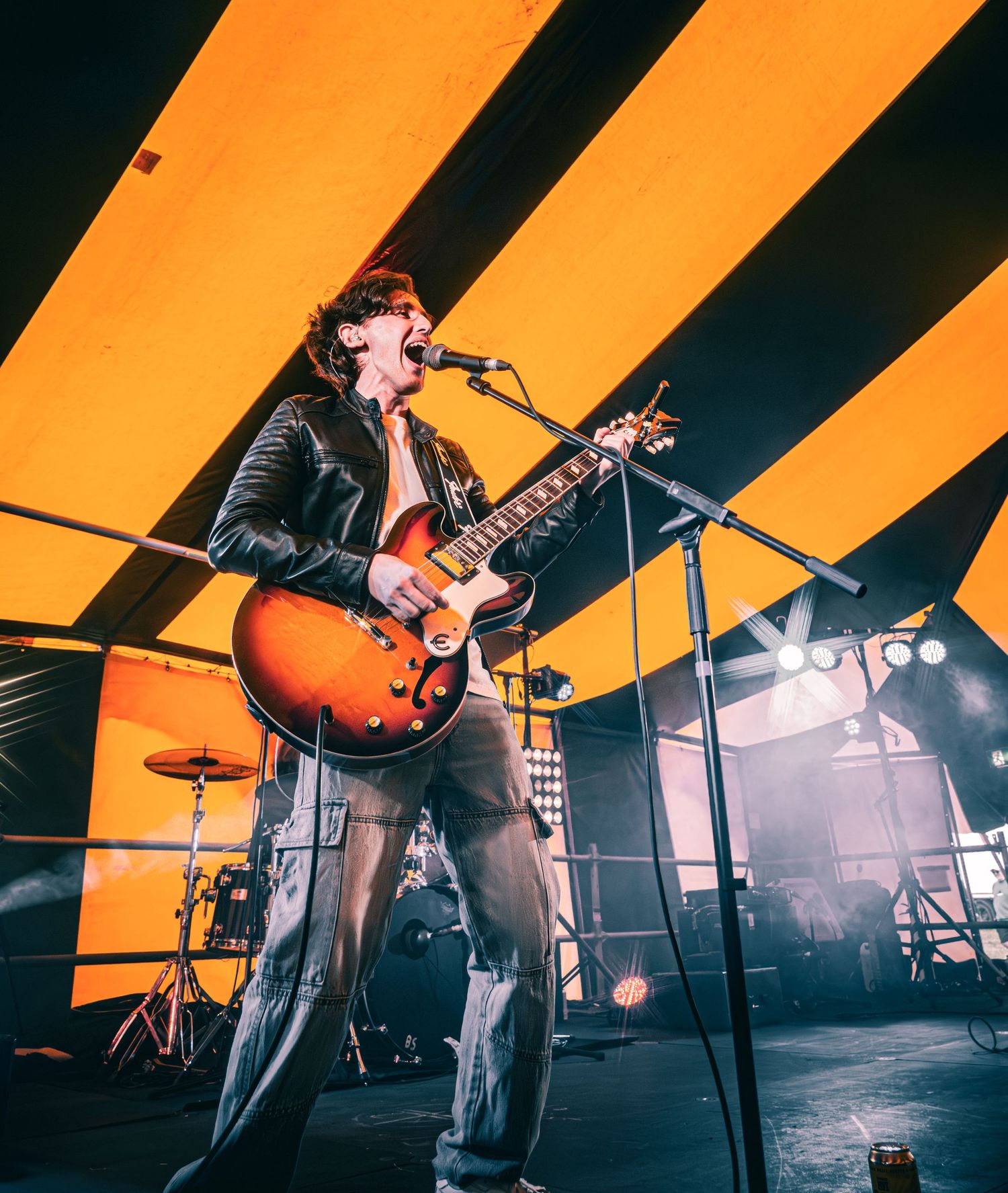 A guitarist singing passionately on stage with a sunburst electric guitar under dramatic yellow lighting.