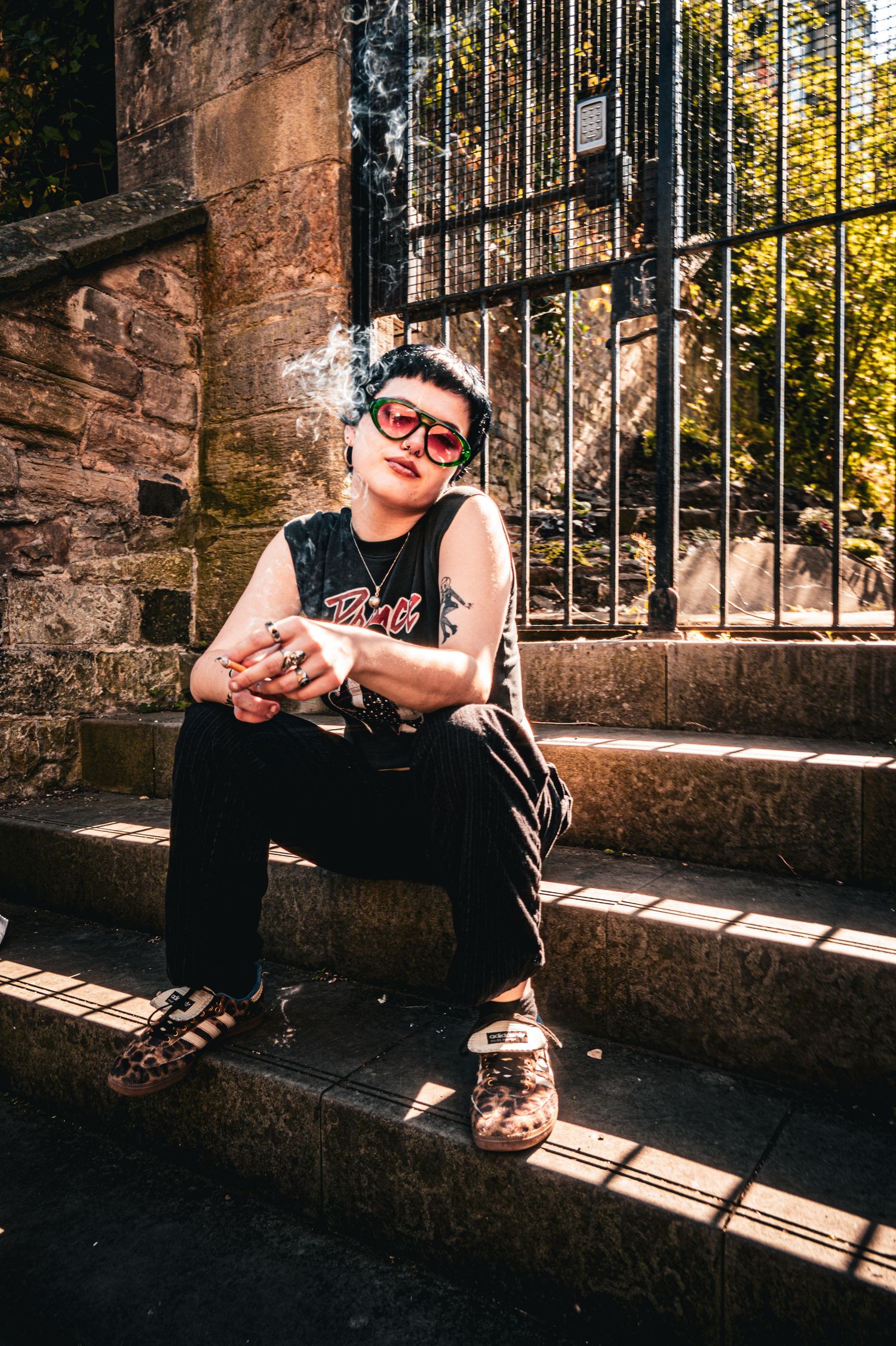 Young woman in red sunglasses sitting on sunny stone steps near iron gate.