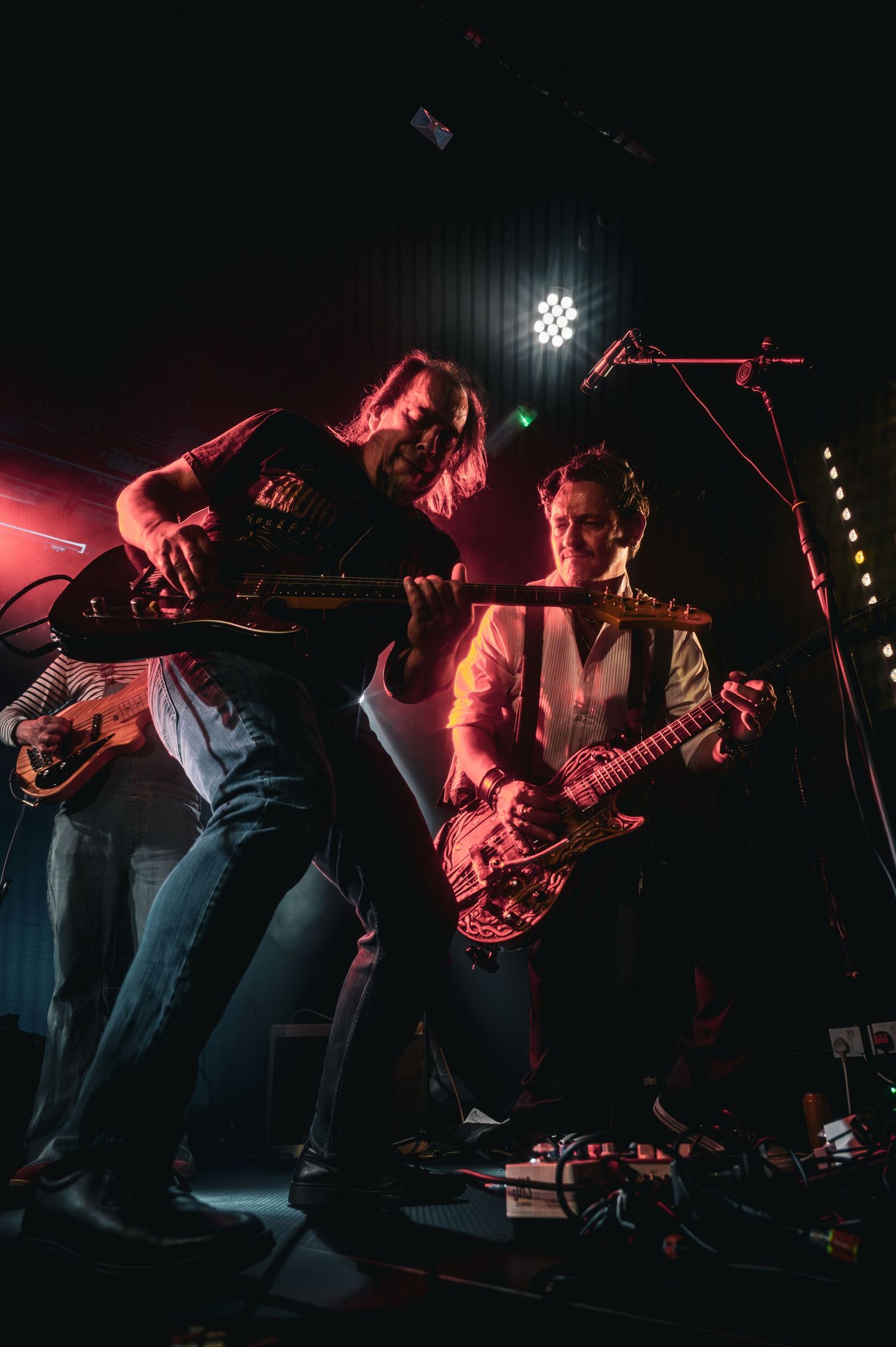 Two guitarists perform energetically on a dark stage under dramatic red and white lighting at a live rock concert.