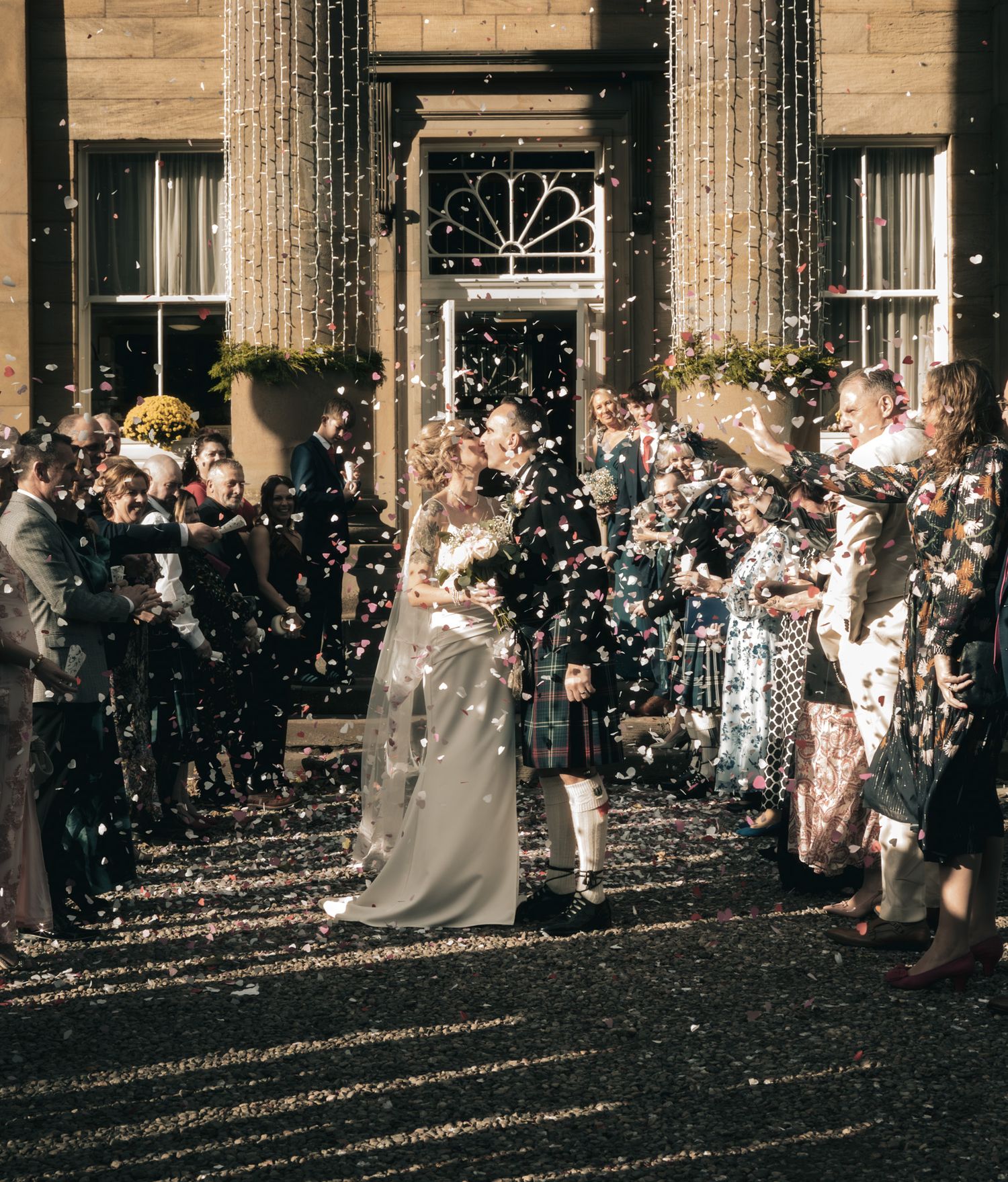 Newlyweds walk through confetti shower outside elegant Scottish manor wedding venue.