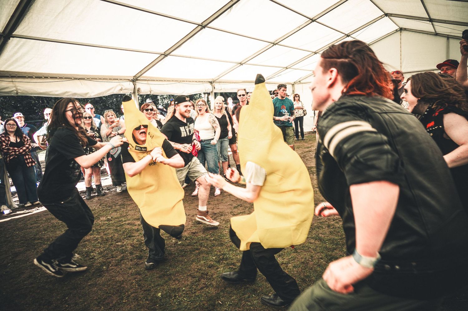 People in banana costumes dancing at an outdoor festival tent party event.