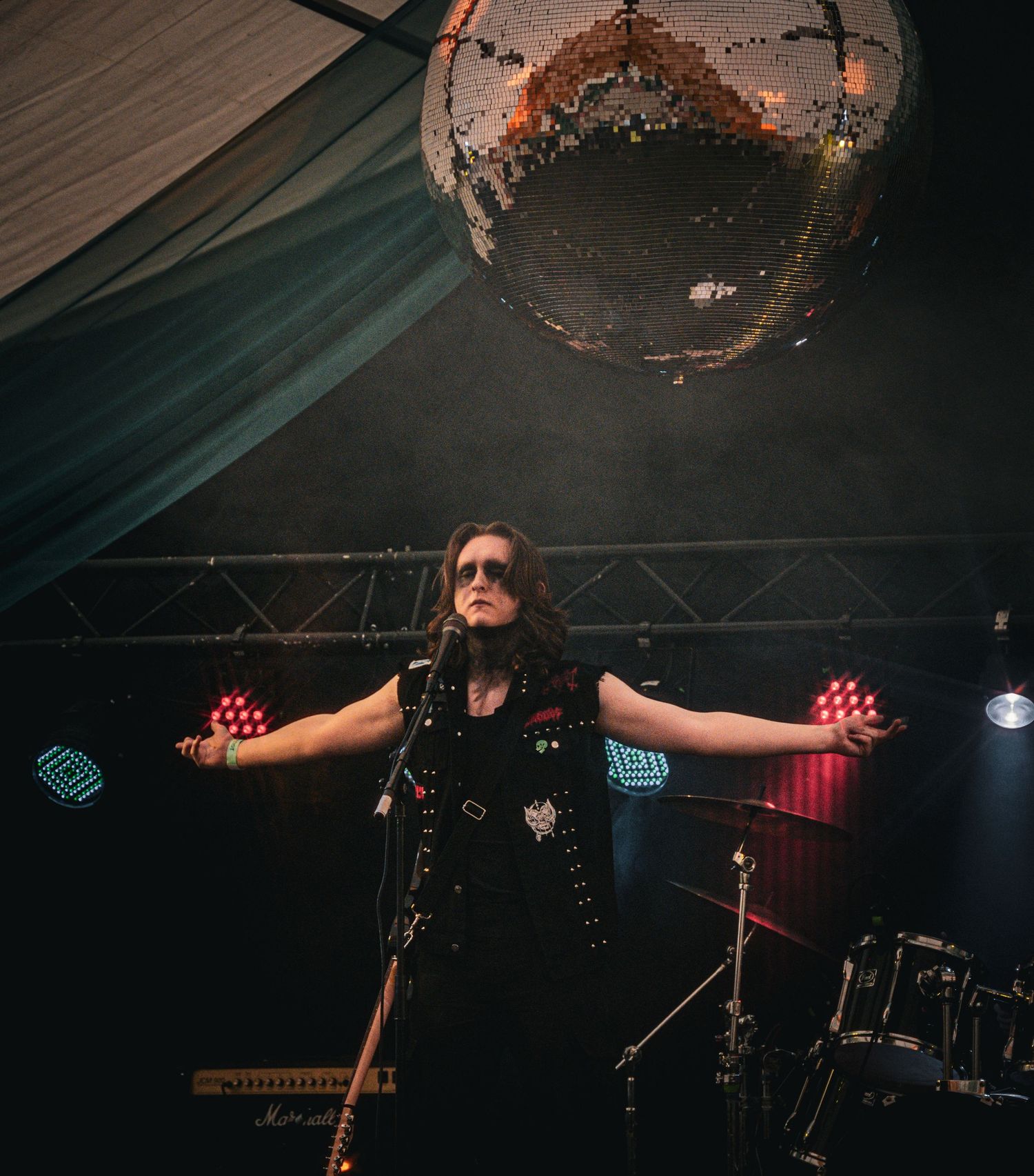 Rock performer with arms outstretched on stage under glowing disco ball with colorful stage lights.
