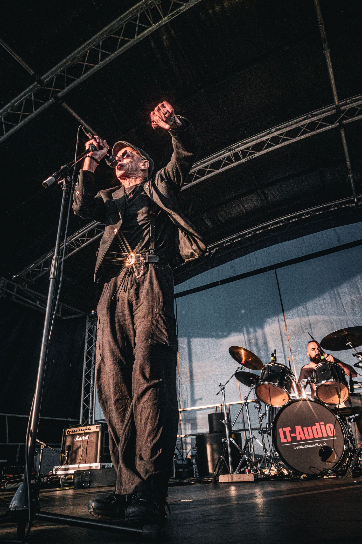 An energetic vocalist in black performs on stage with a drummer and LT-Audio kit behind him.
