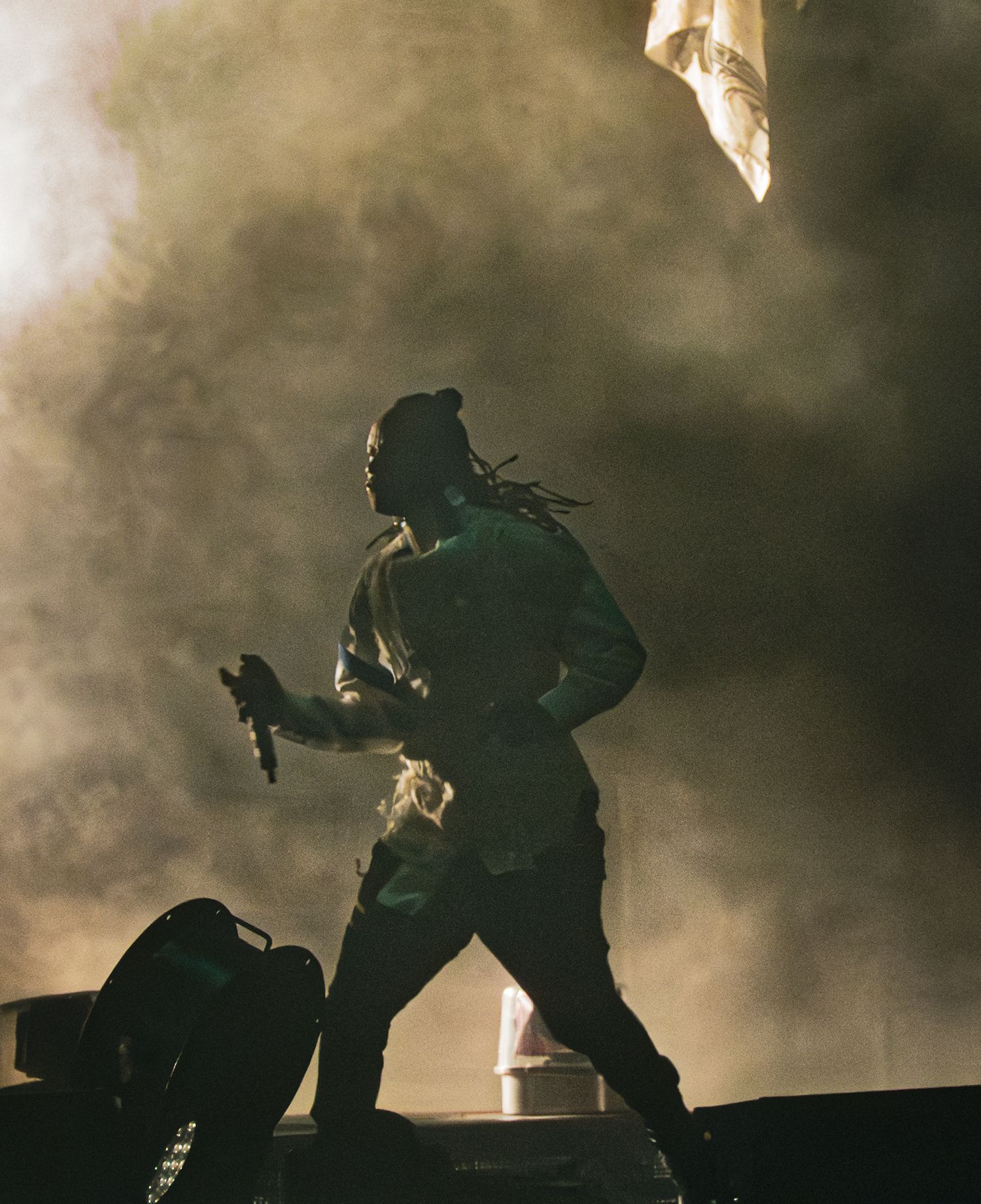 Silhouetted performer with dreadlocks on stage surrounded by dramatic fog and moody green lighting at a live concert.