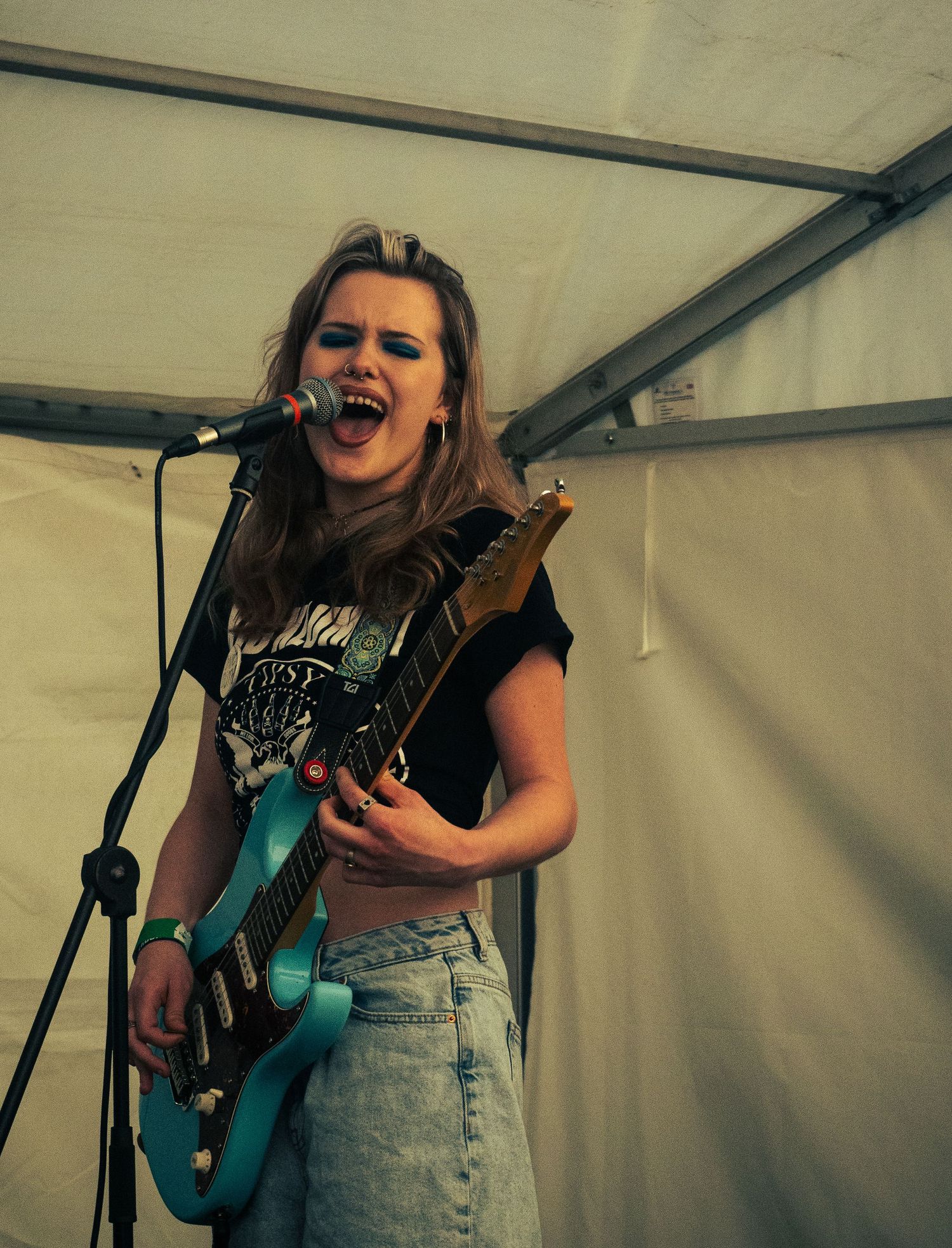 Musician singing passionately while playing teal electric guitar during festival performance.