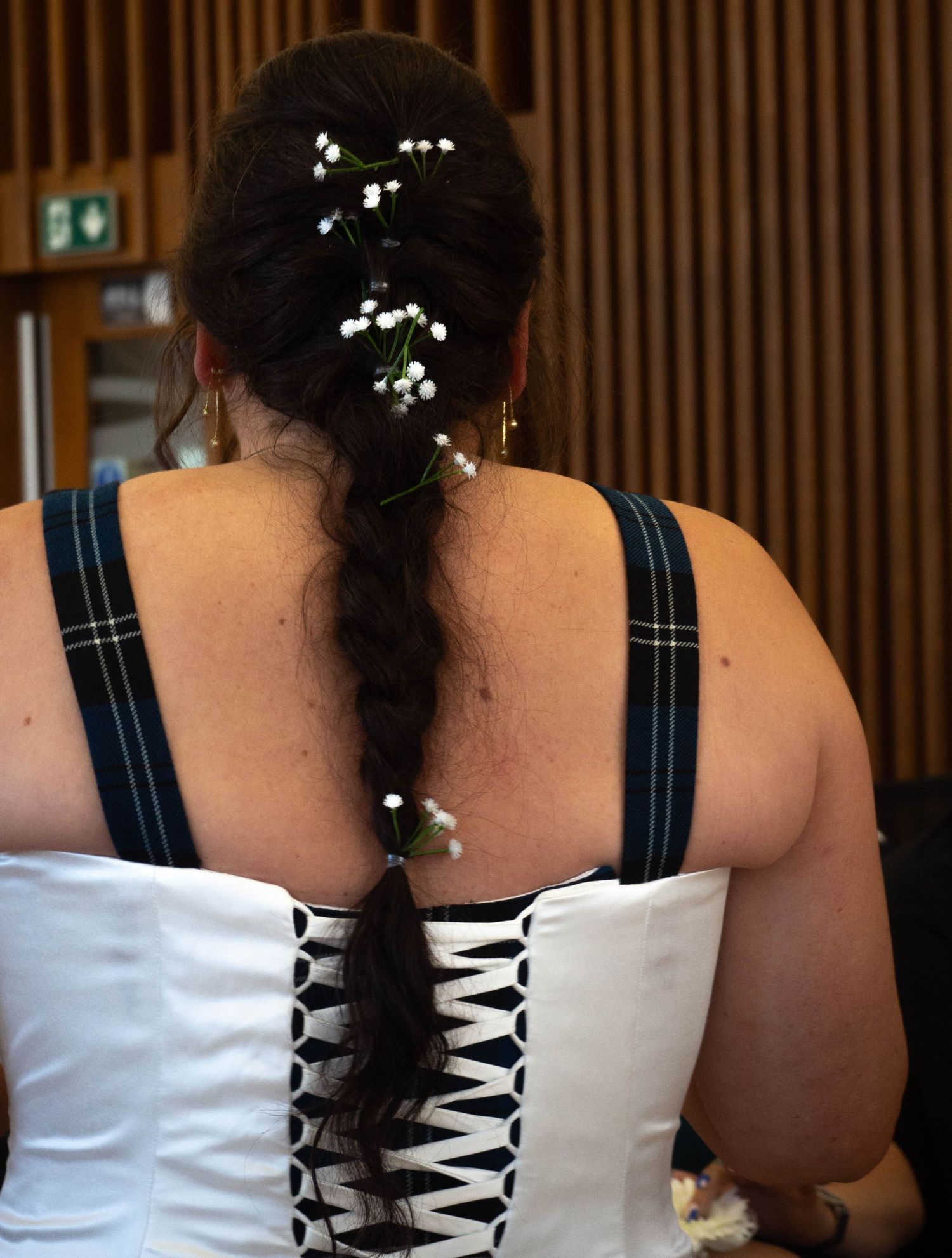 Bride with dark braided hair adorned with delicate white baby's breath flowers, wearing a white and black laced corset wedding dress.