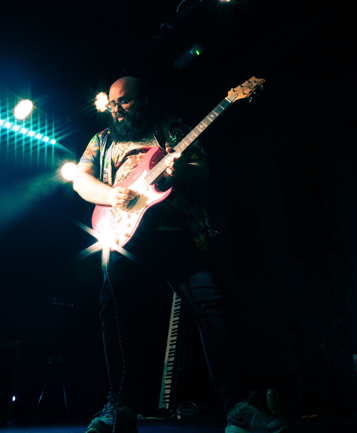 A guitarist performs on stage with dramatic blue lighting and starburst lens flares creating an atmospheric concert scene.