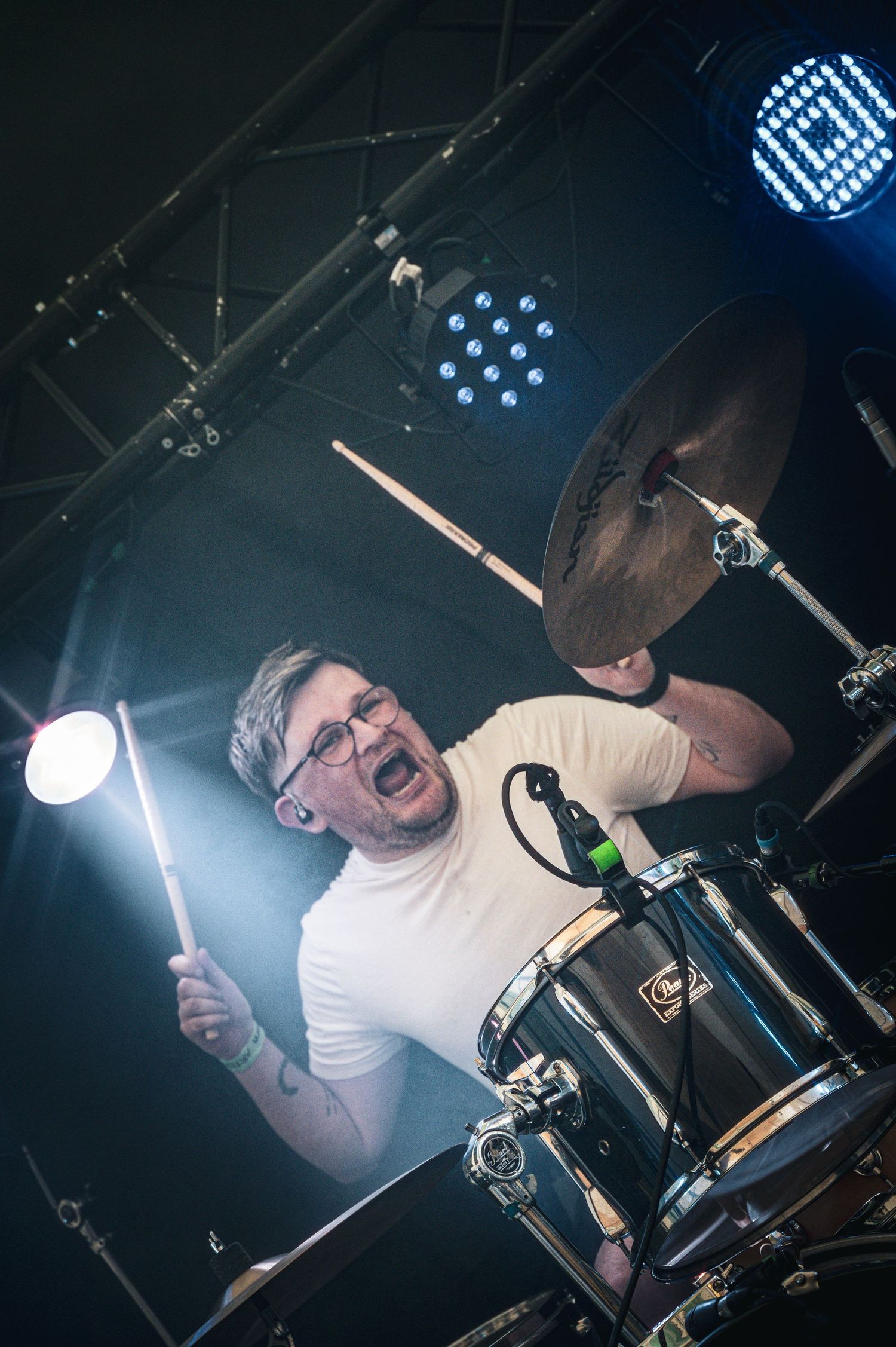 Energetic drummer playing cymbals under blue stage lights with drumsticks mid-strike.