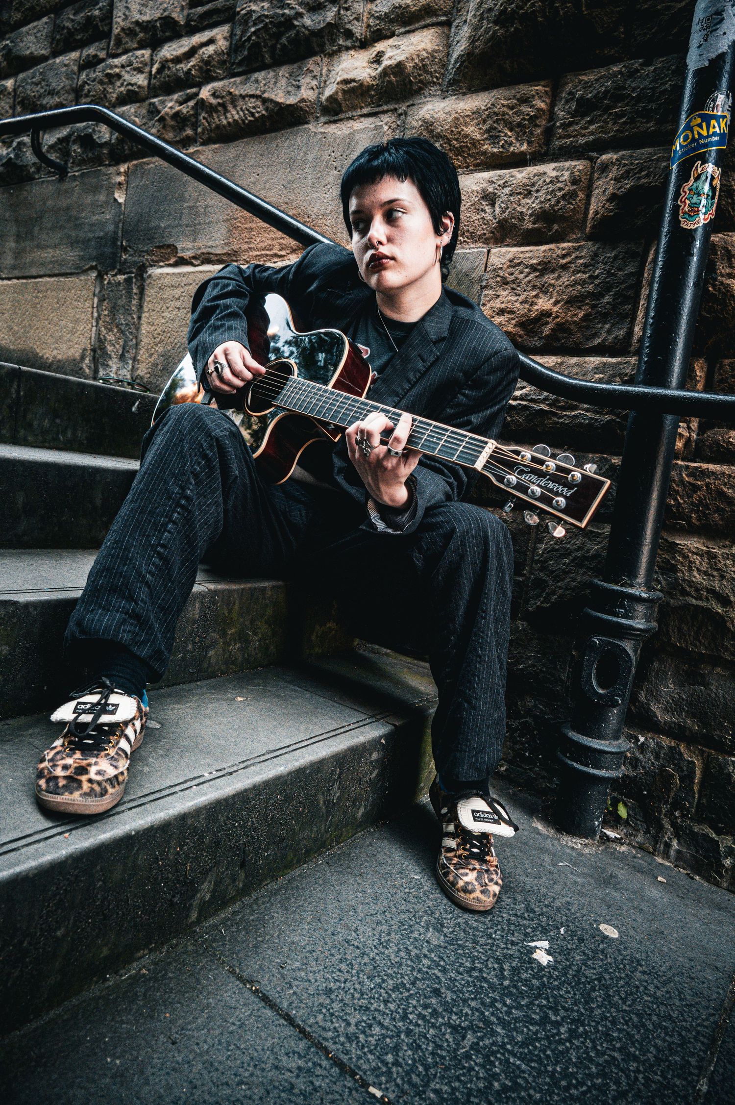 Young musician playing acoustic guitar on urban stone steps wearing leopard print sneakers.