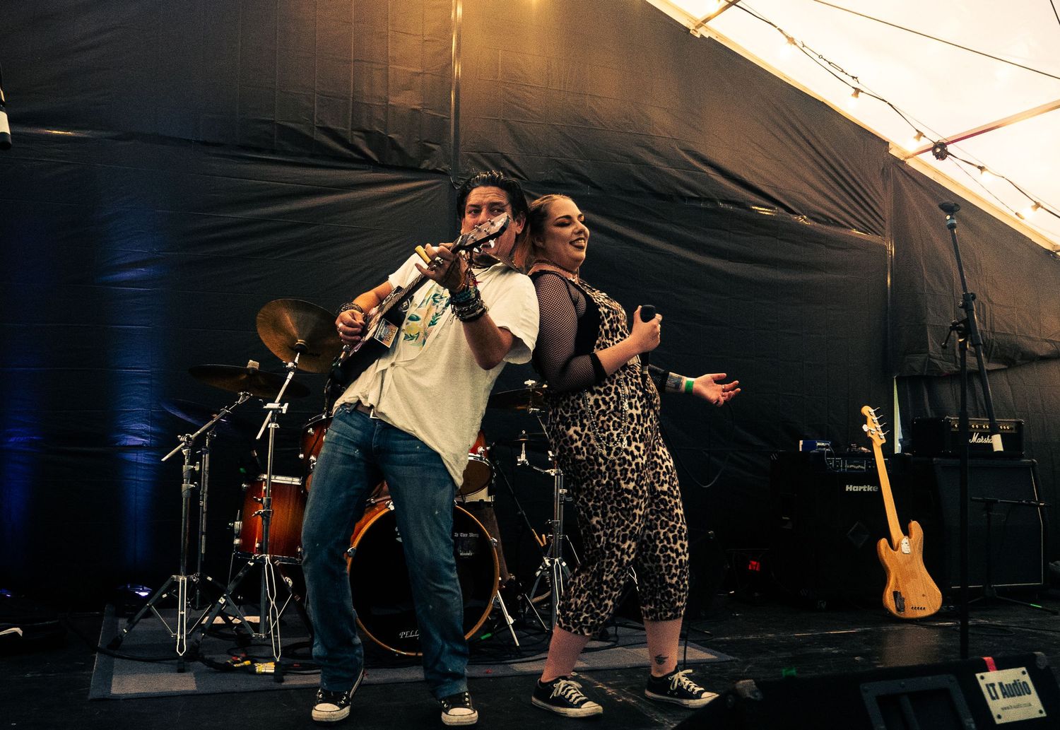 Two energetic performers dancing and singing together on stage during a live concert performance.