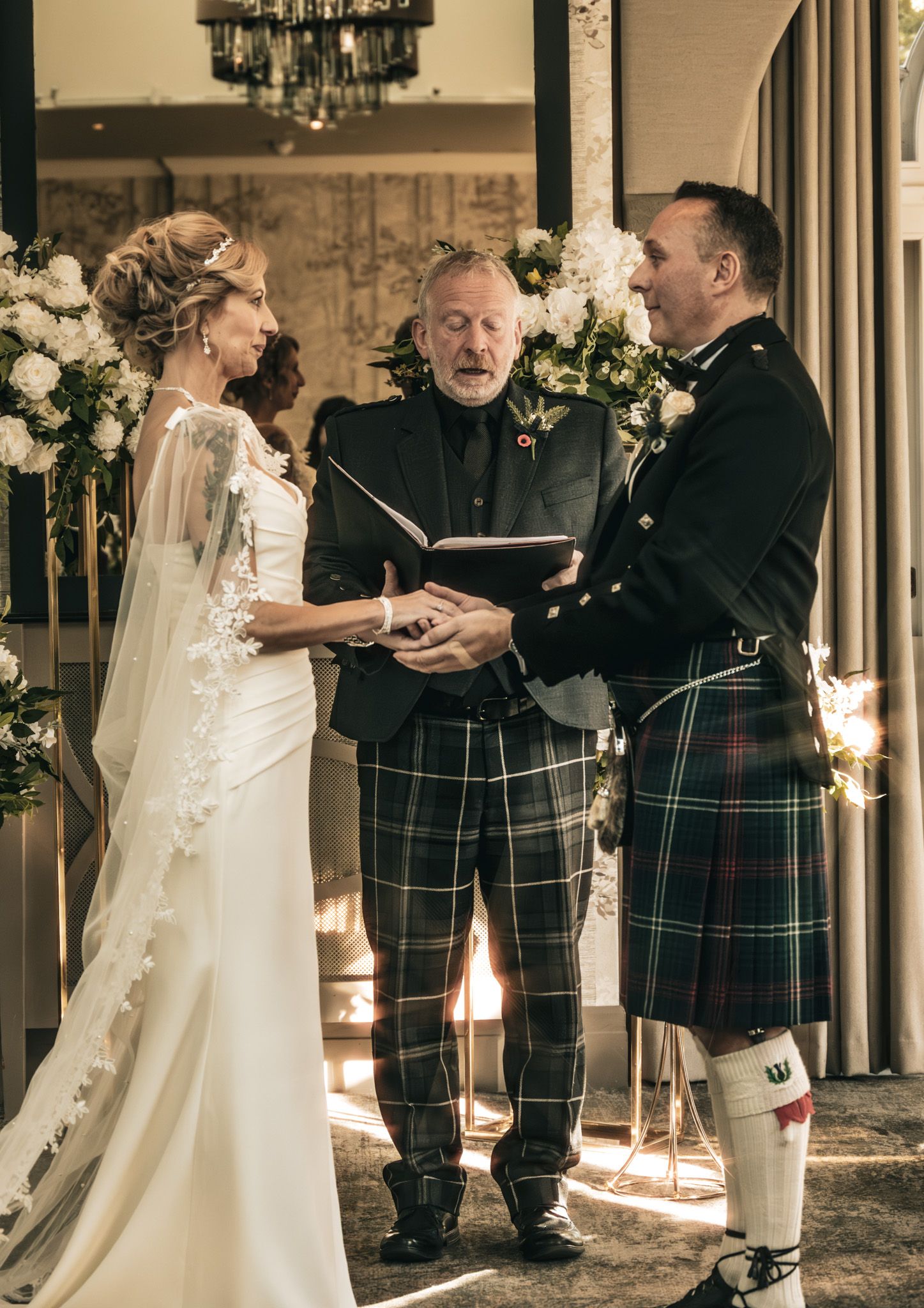 Bride and groom exchange vows at Scottish wedding ceremony, groom wearing traditional tartan kilt.